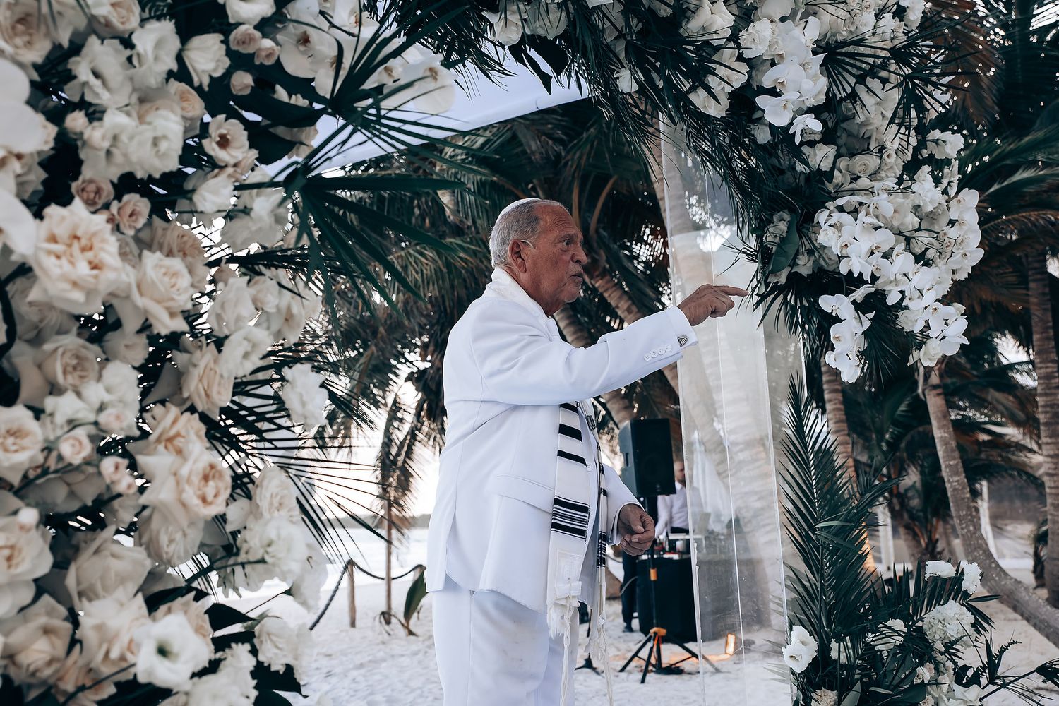 Elegant wedding ceremony arch decorated with white flowers and palm leaves.