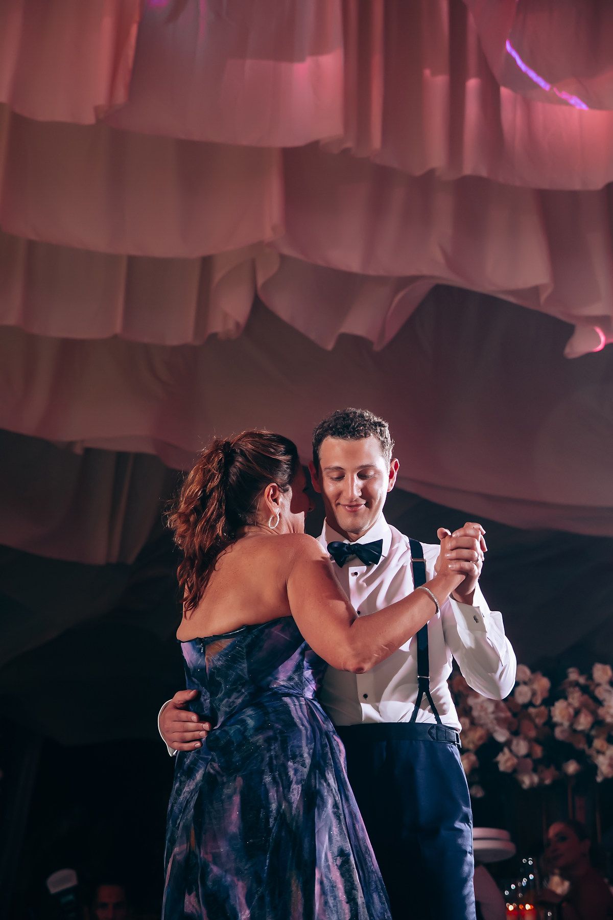 Couple dancing together under romantic pink lighting at wedding reception.