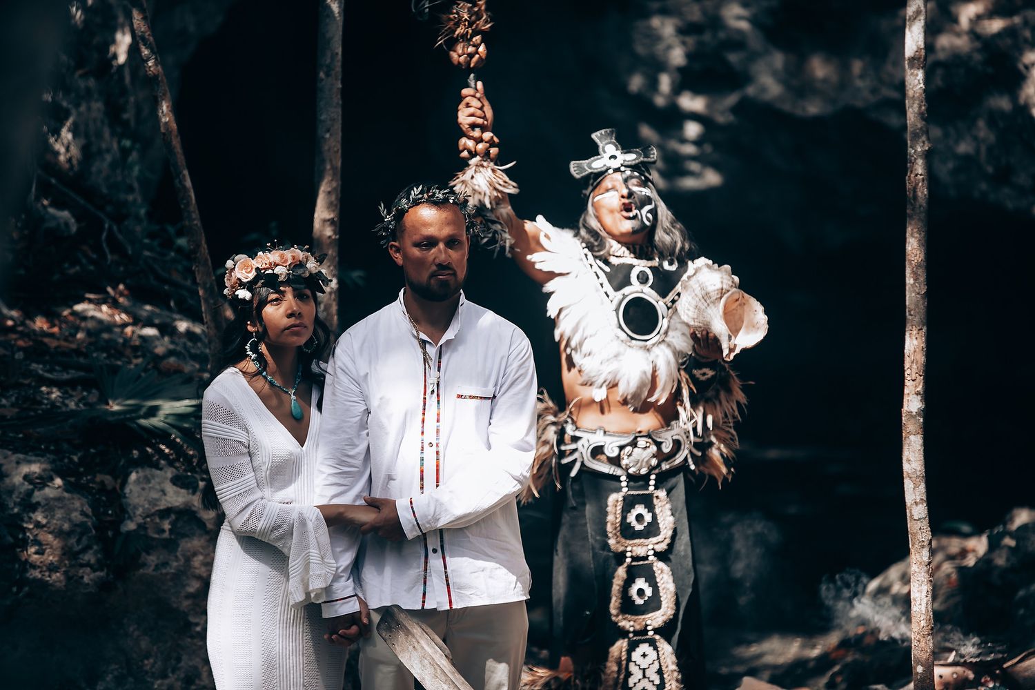 Traditional ceremony participants in white attire and headdresses gathered in nature.