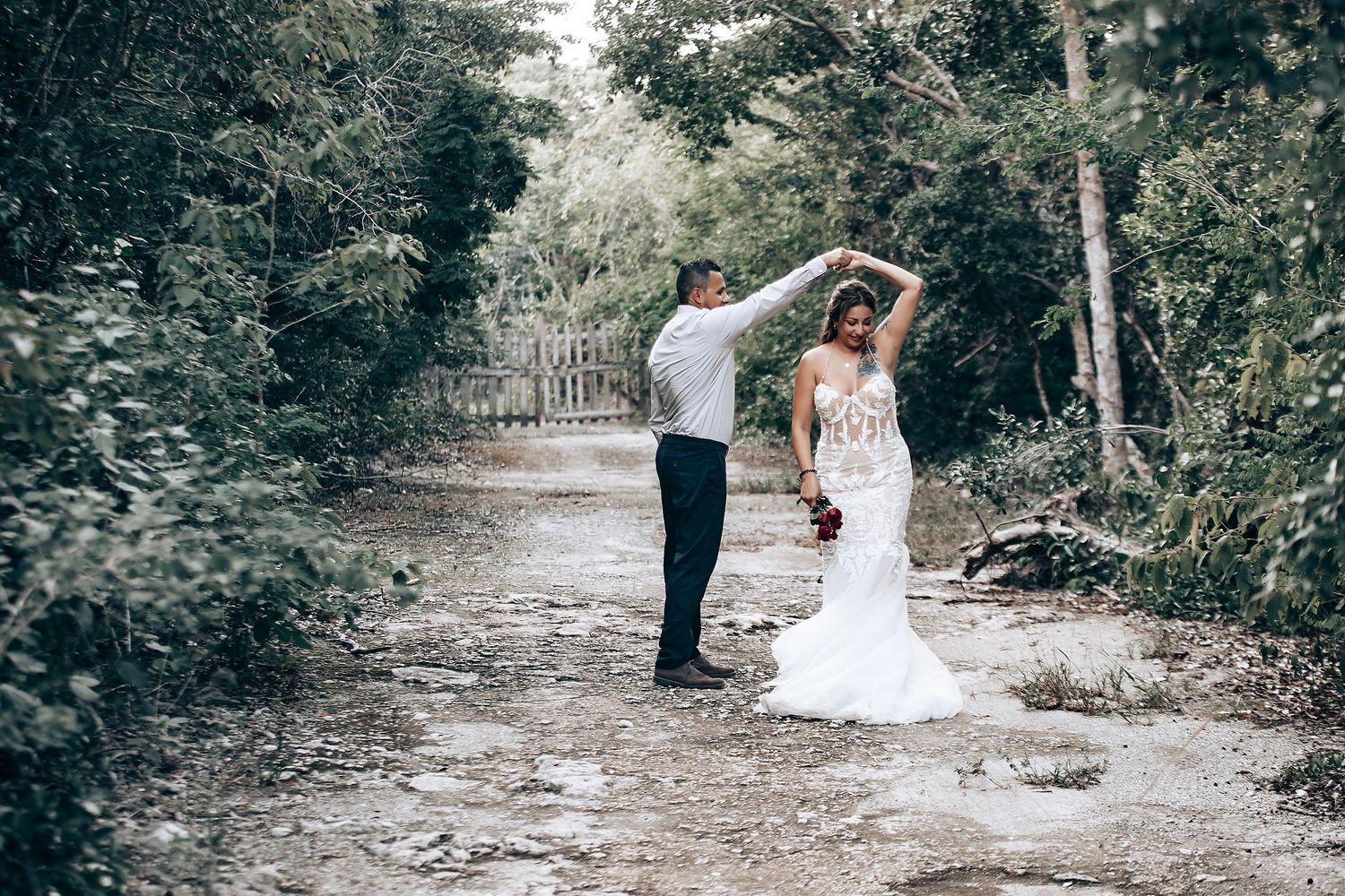 Newlyweds dancing together on a wooded path surrounded by green foliage.
