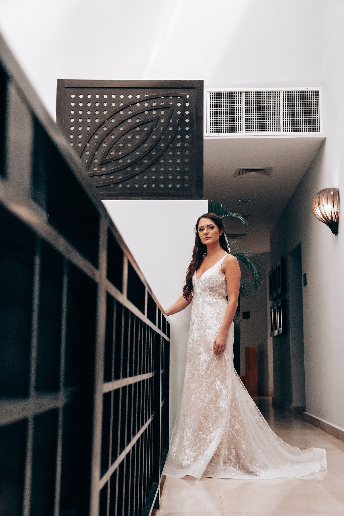 A stunning lace wedding dress is showcased in an elegant hallway with modern architectural details.