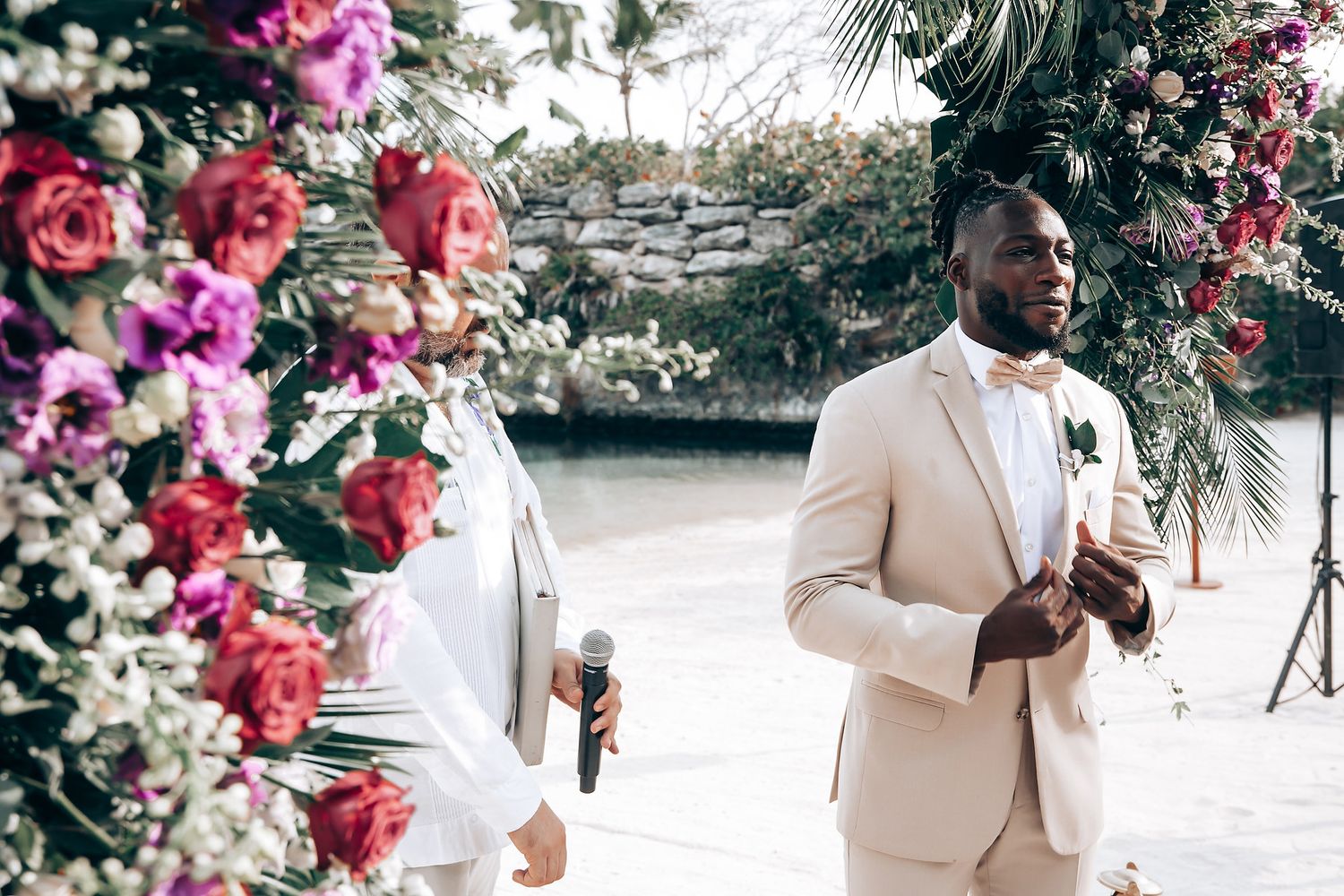Wedding party poses under floral arch with pink and red blooms in outdoor garden setting.