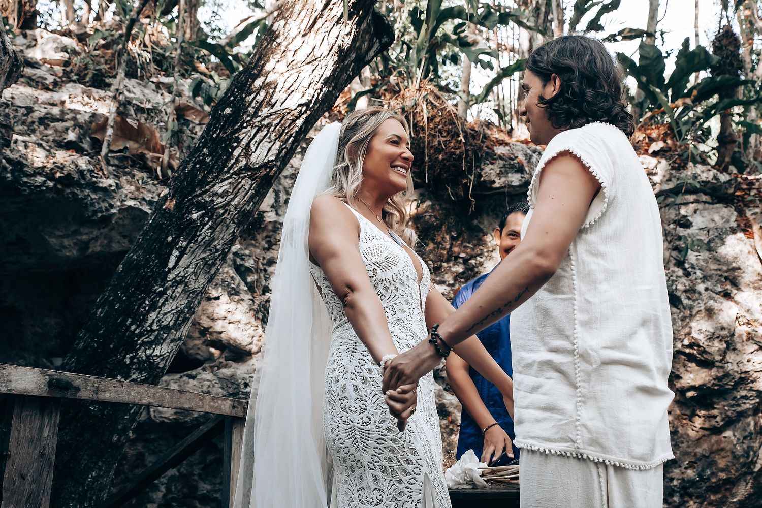 A couple shares an intimate moment in a garden setting wearing white outfits during their wedding celebration.