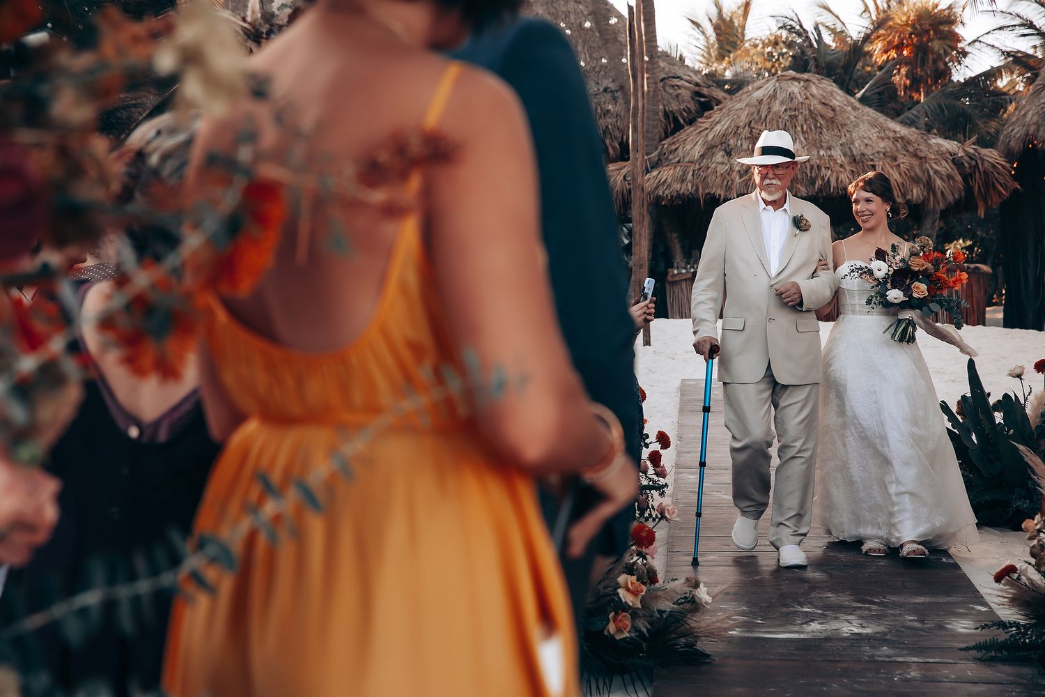 Tropical beach wedding ceremony setup with palm trees and guests in white attire.