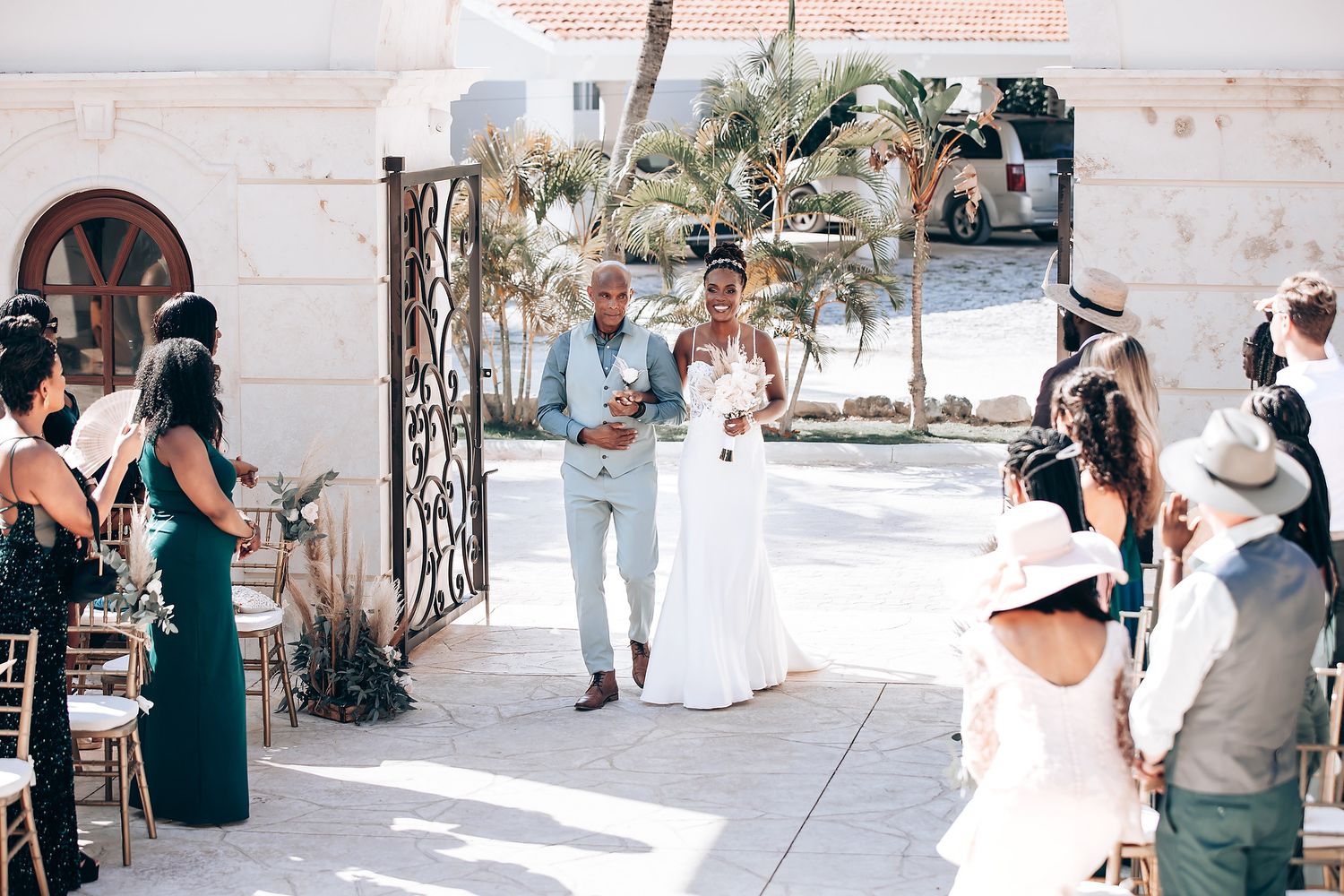 Wedding guests gathered at an elegant outdoor venue with white decor and palm trees.