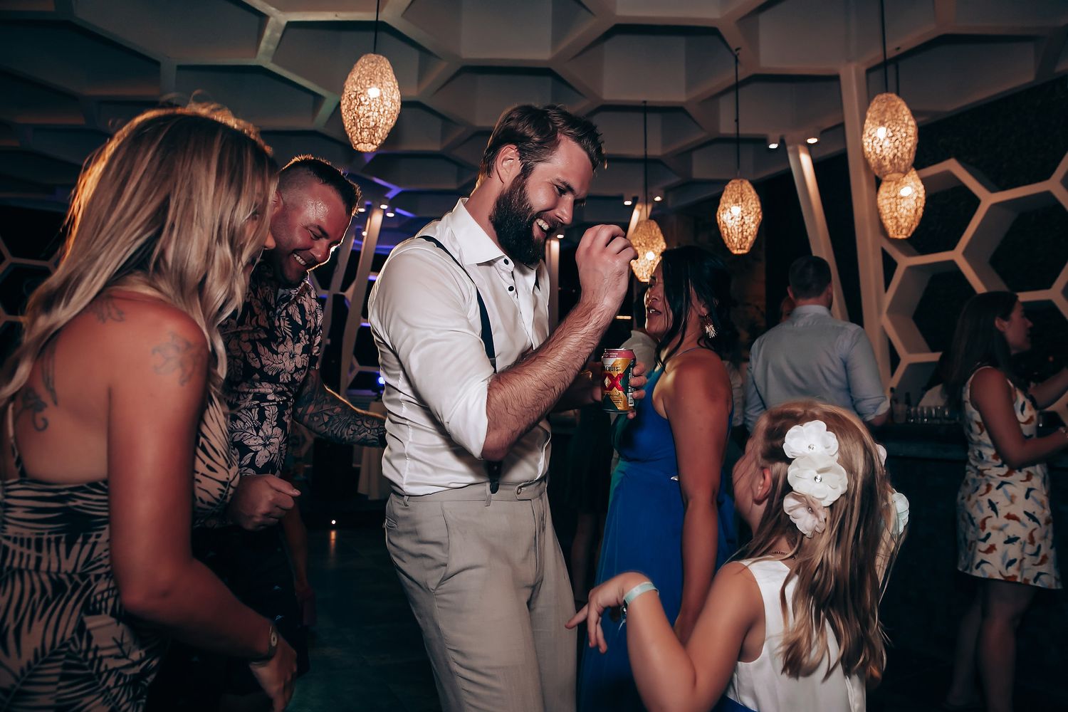 Wedding reception dance floor filled with guests under geometric ceiling patterns and mood lighting.
