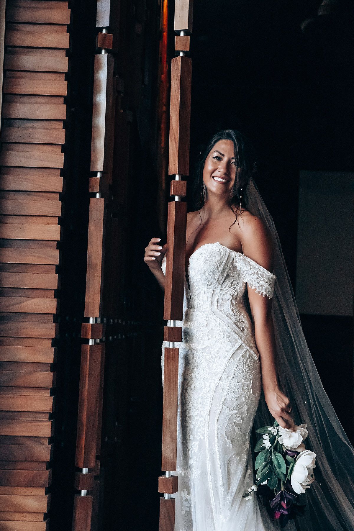 Bride in a stunning lace wedding gown poses near wooden shutters.