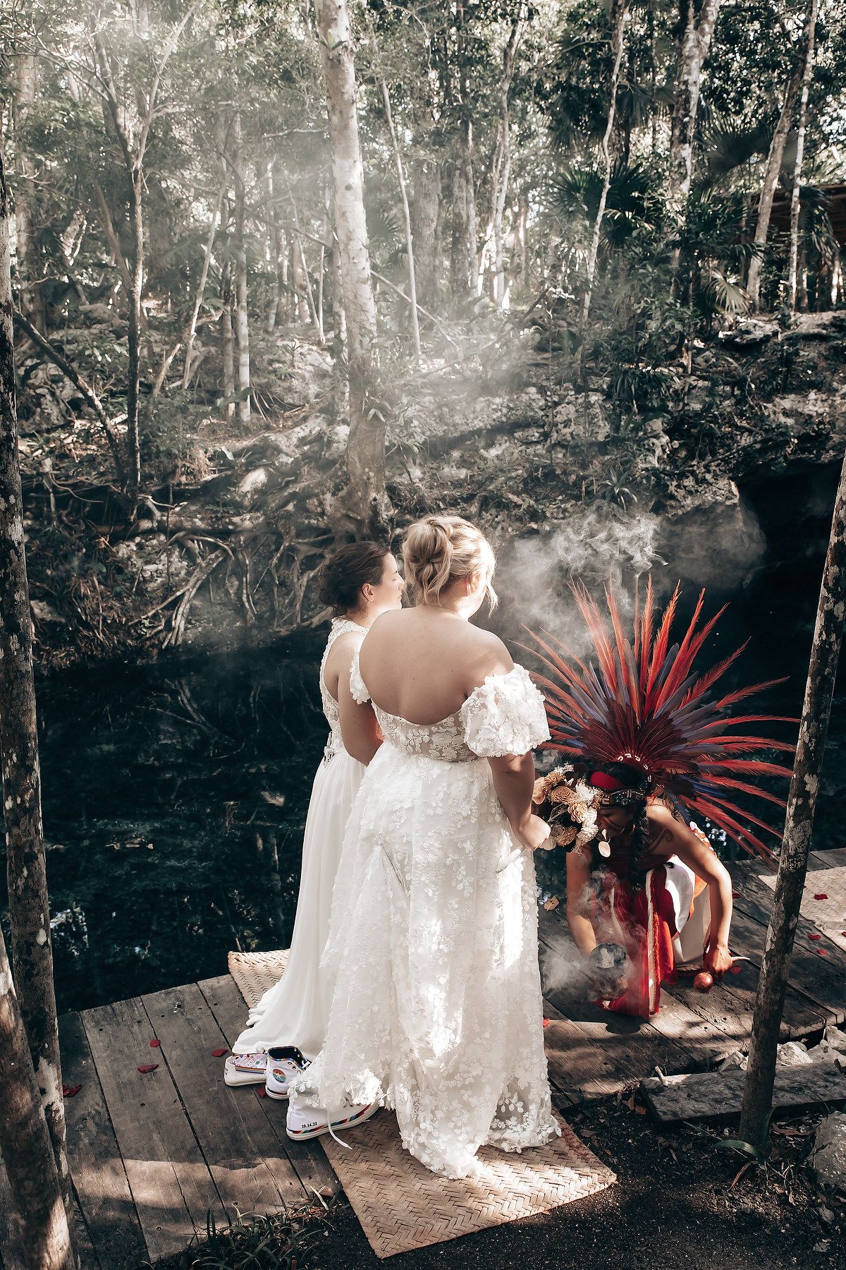 A couple in wedding attire standing in a lush, forested environment with sunlight filtering through the trees.