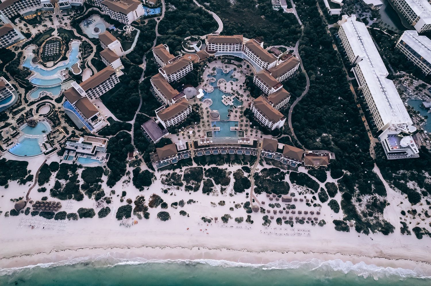 Aerial view of a large resort complex with a central courtyard, surrounded by buildings and amenities along a beach.
