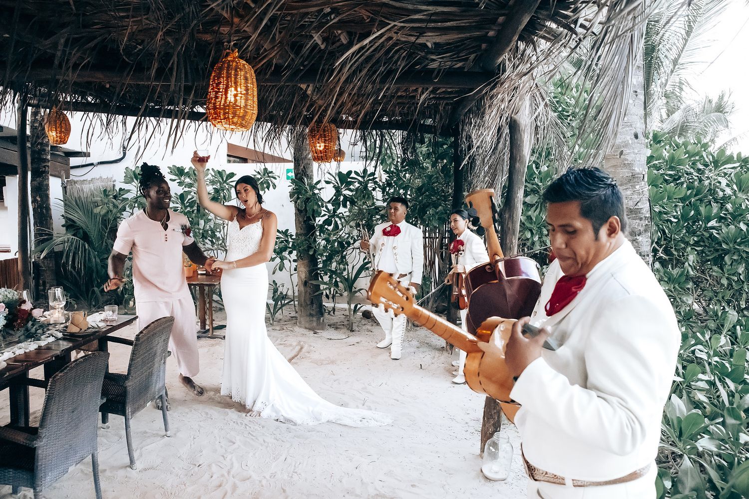 A bride and groom stand under a floral arch on a beach.