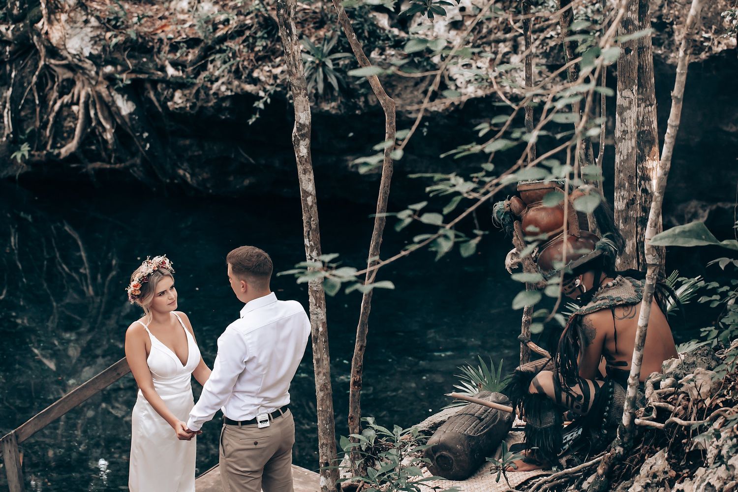 A romantic forest photoshoot scene with a couple standing among trees and rocks.