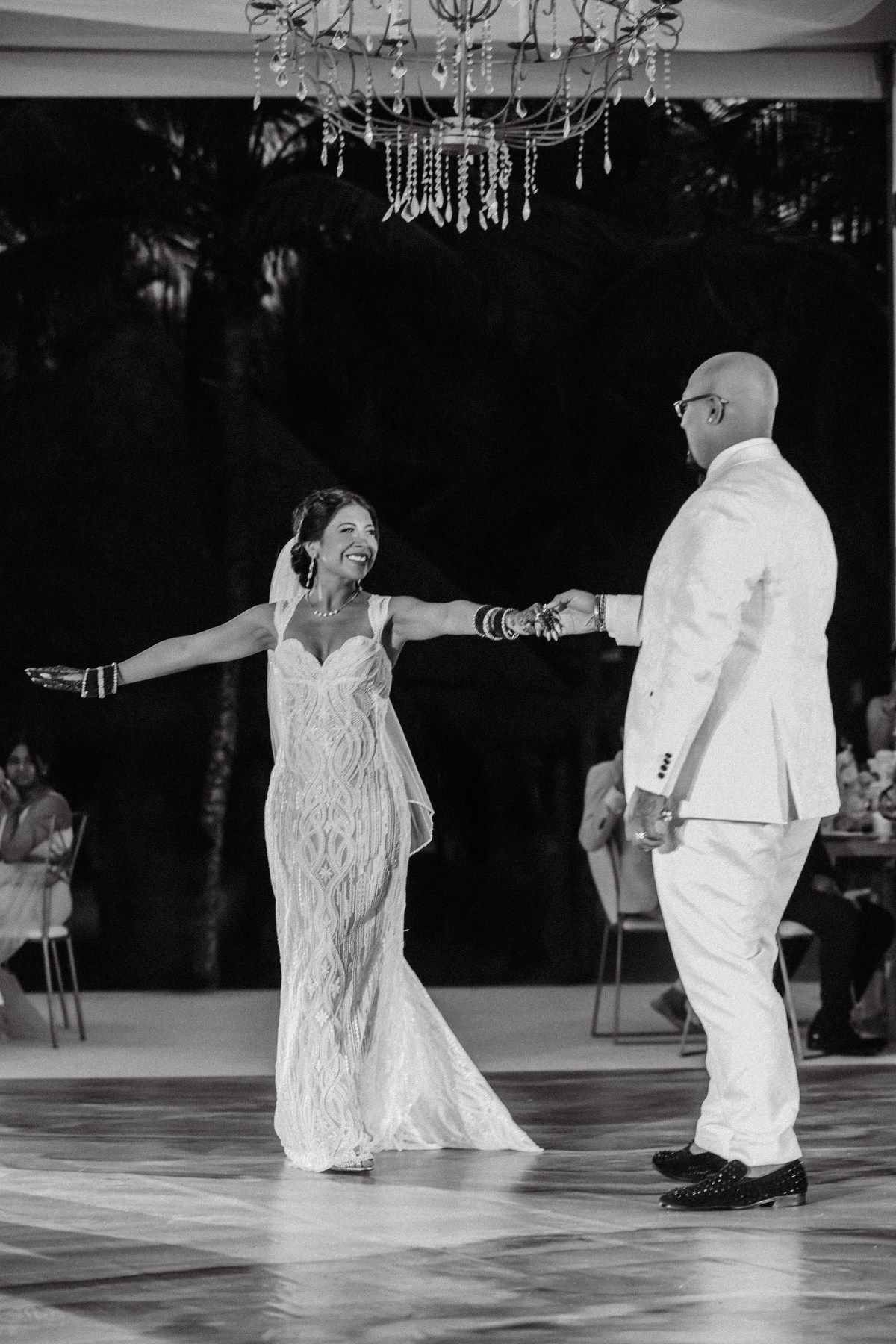 Black and white photo of bride and groom sharing first dance under crystal chandelier at wedding reception.