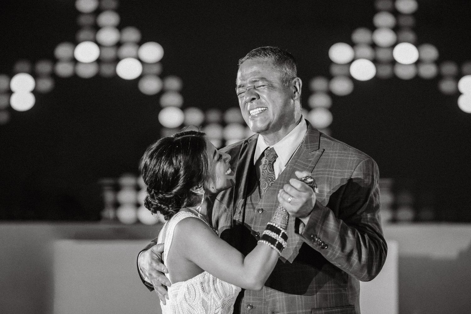 Black and white photo of a bride and older man sharing an emotional father-daughter dance at a wedding reception.