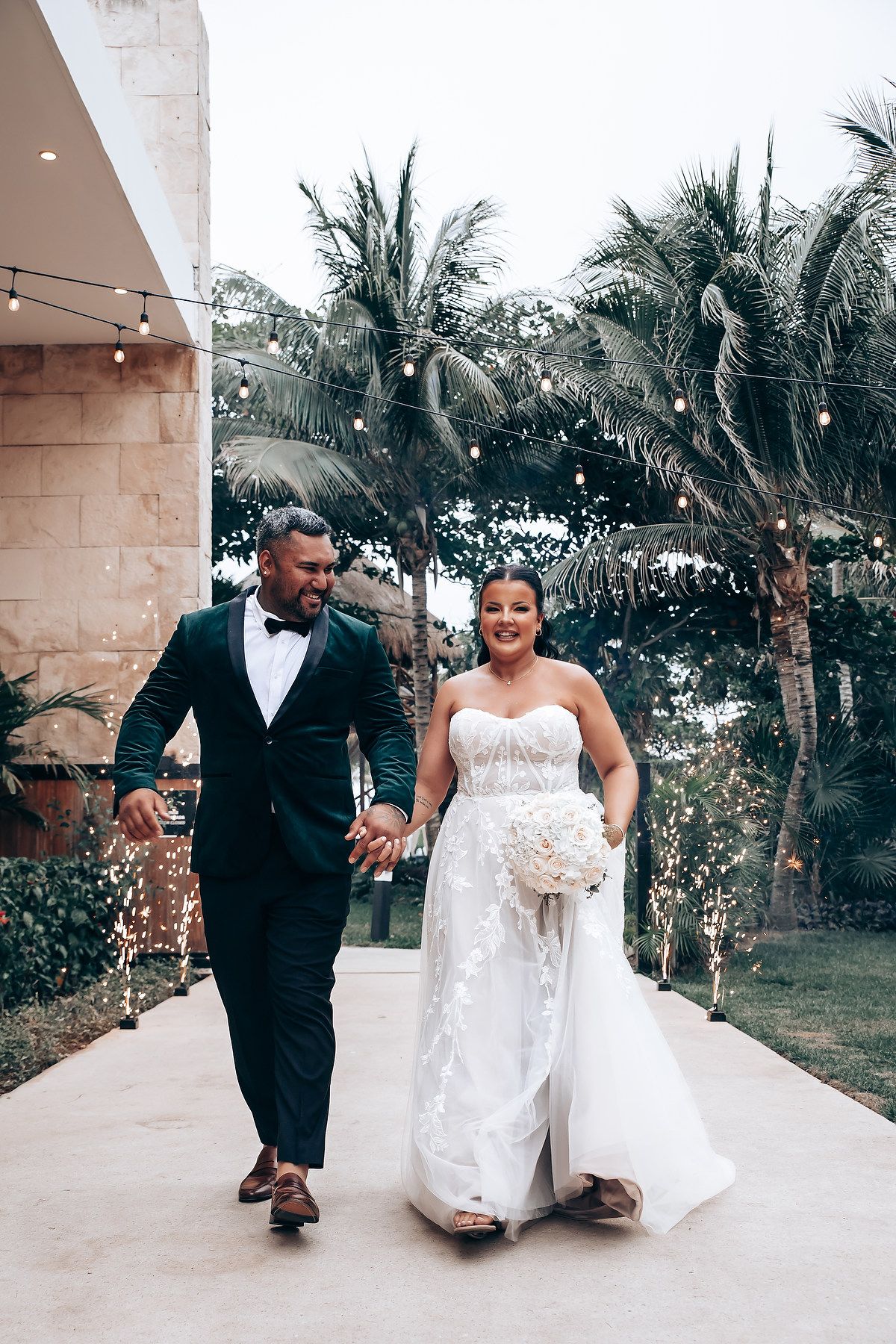 Couple in formal attire dancing together on outdoor patio with palm trees.