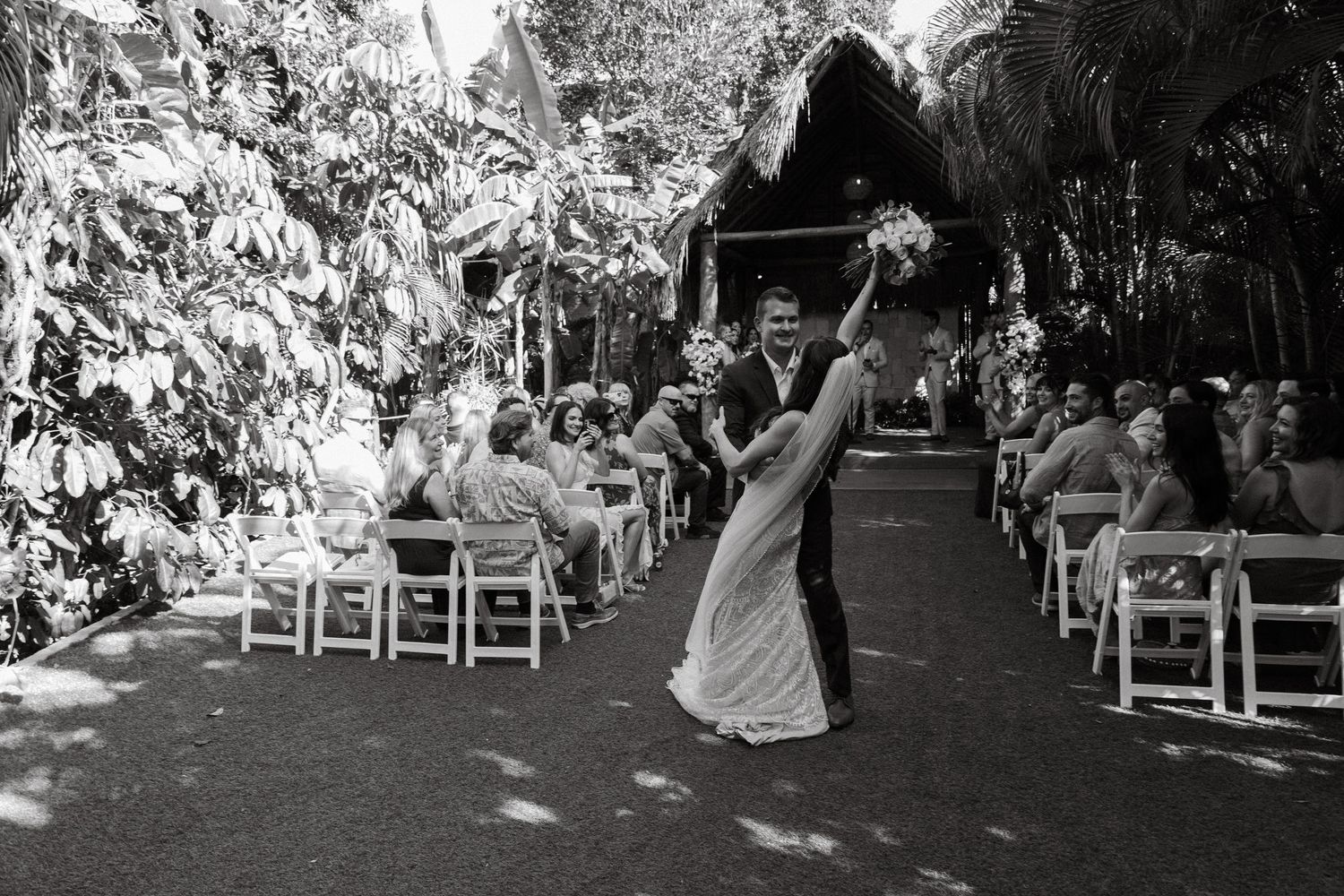 Newlyweds celebrate in black and white photo walking down outdoor aisle after ceremony.
