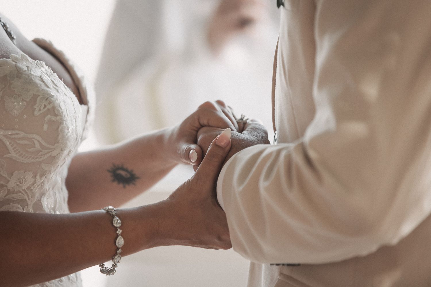 Close-up of bride and groom holding hands during wedding ceremony, bride wearing lace dress and diamond bracelet.