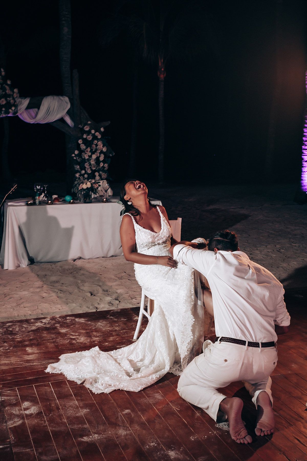 A joyful wedding moment captured on a wooden dance floor with decorative lighting.