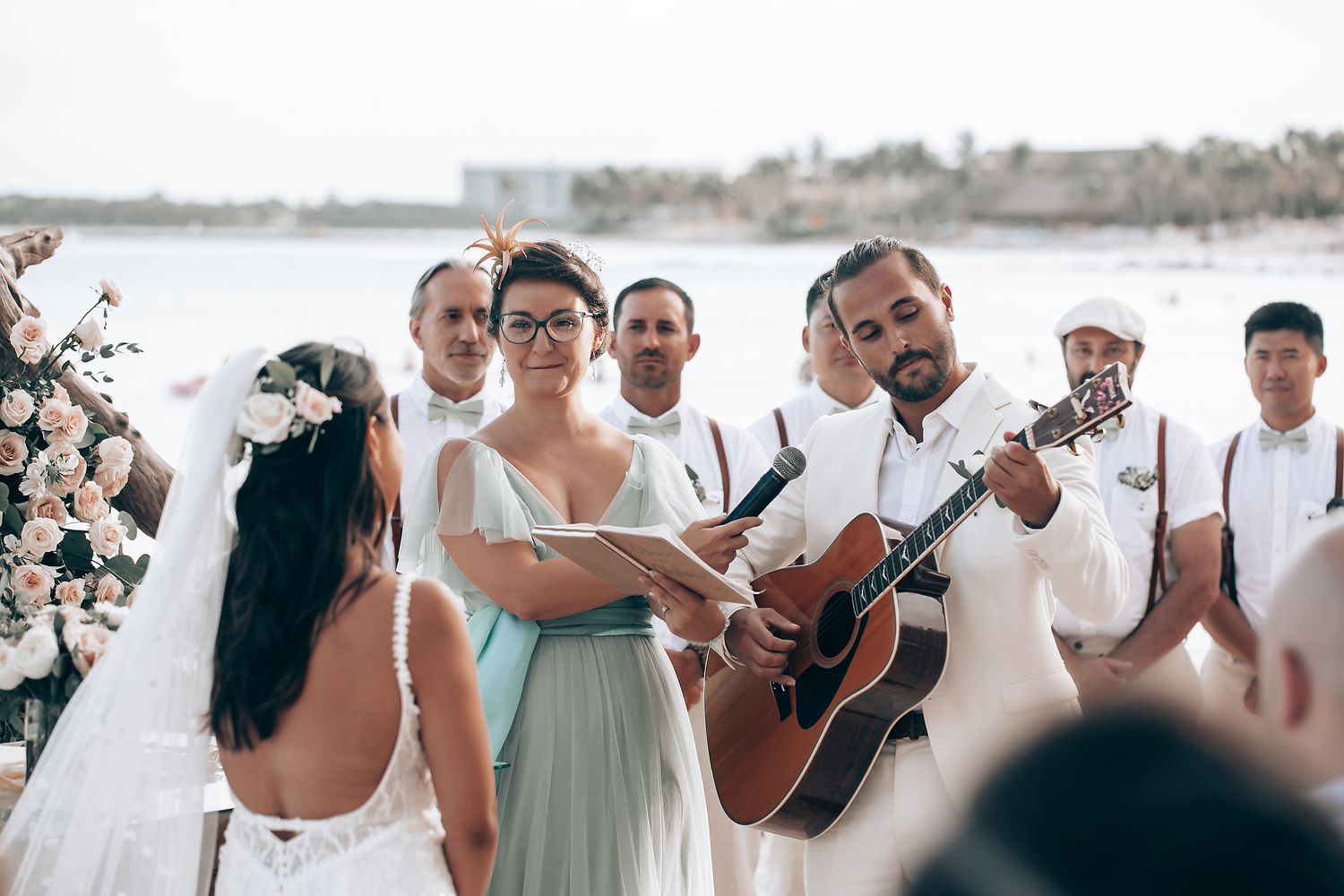 Wedding party performing music and celebrating on a beach with acoustic guitar.