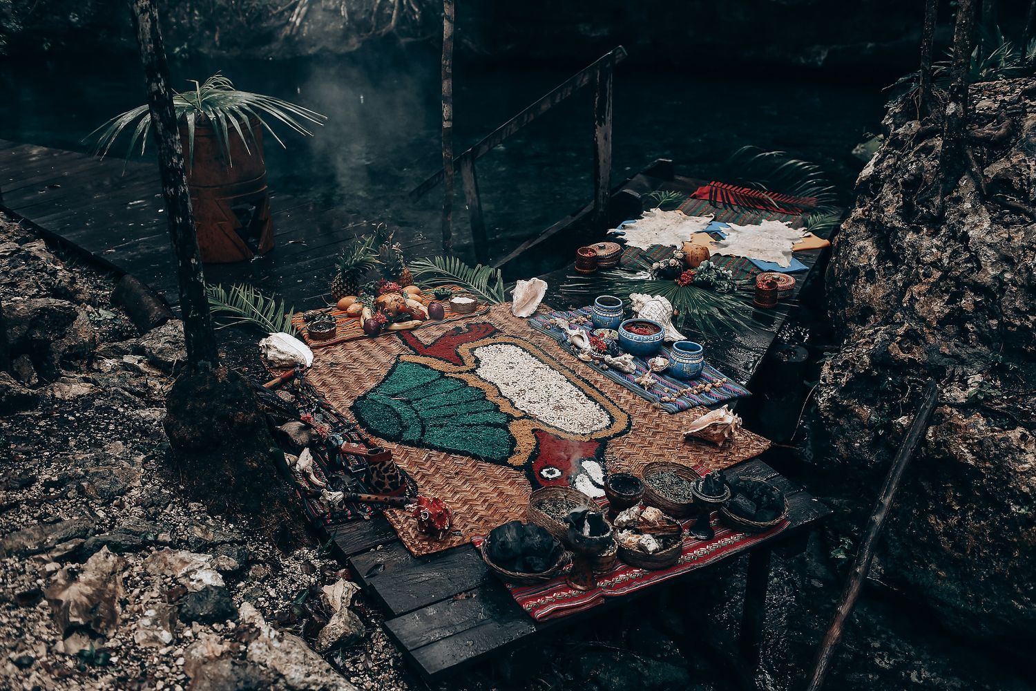 Group of people gathered outdoors in a tropical setting with blankets and decorations for a celebration.