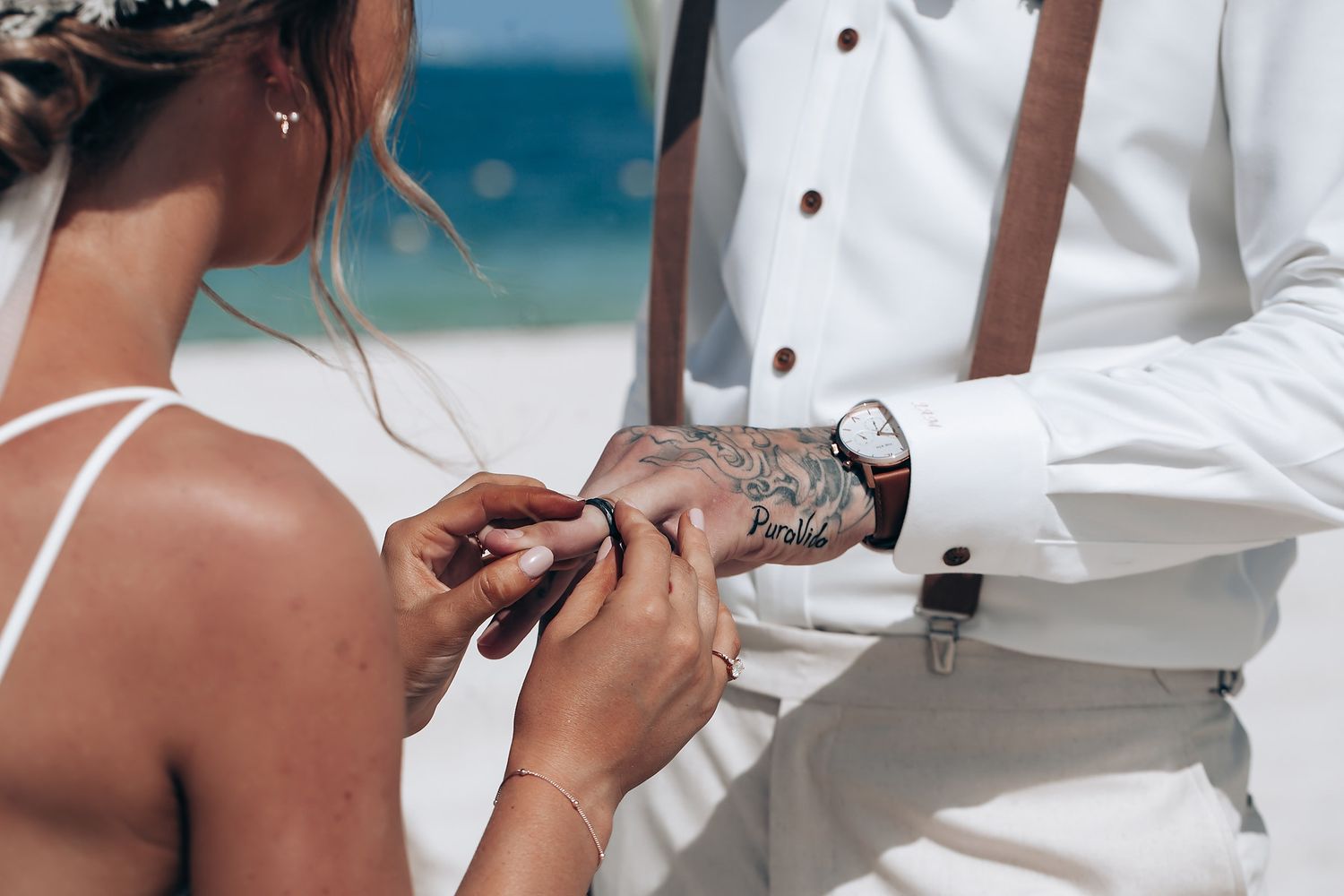 Wedding party dressed in crisp white outfits gathered on a sunny beach.