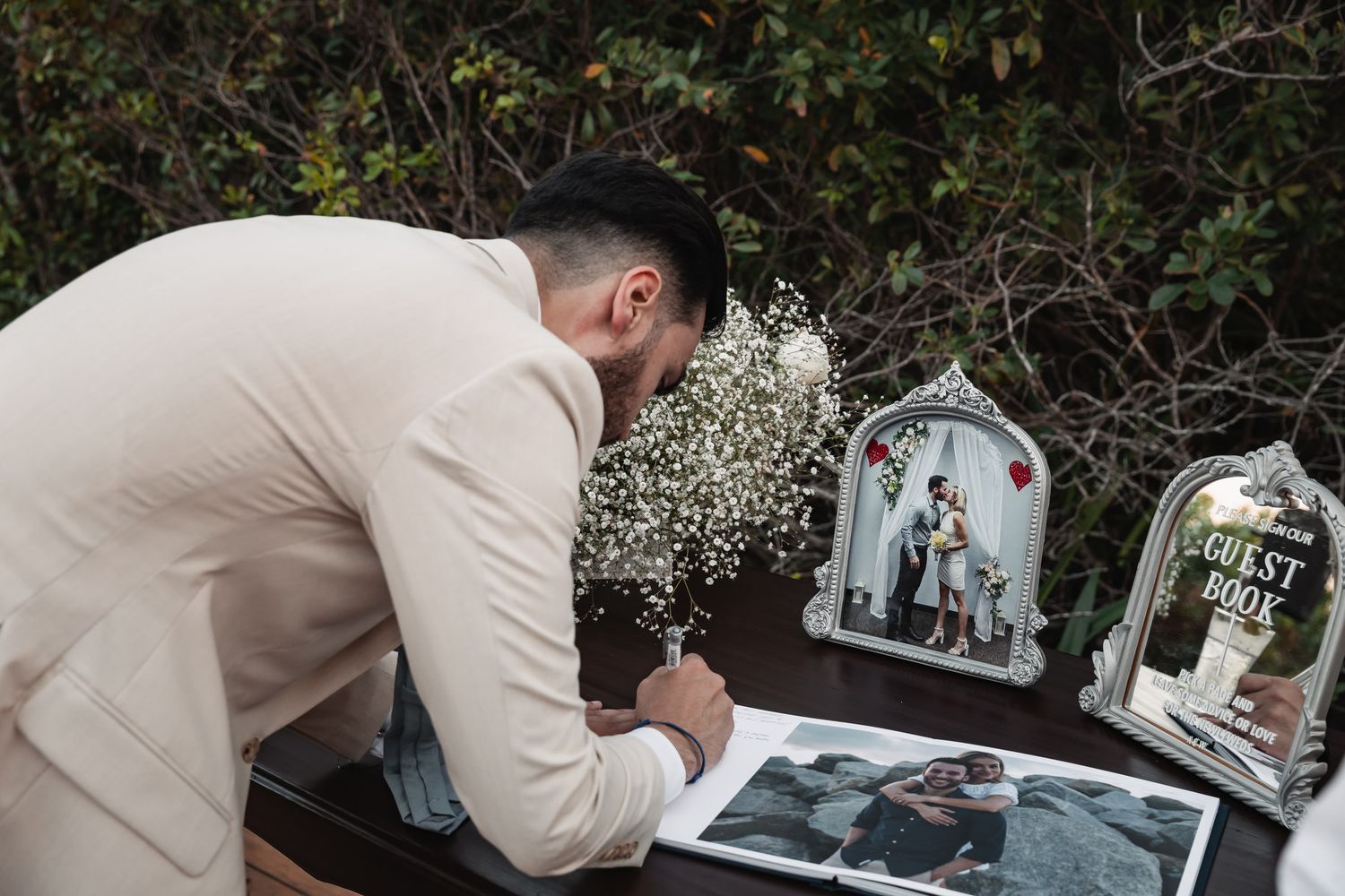 Guest signing wedding guest book at table decorated with baby's breath flowers.