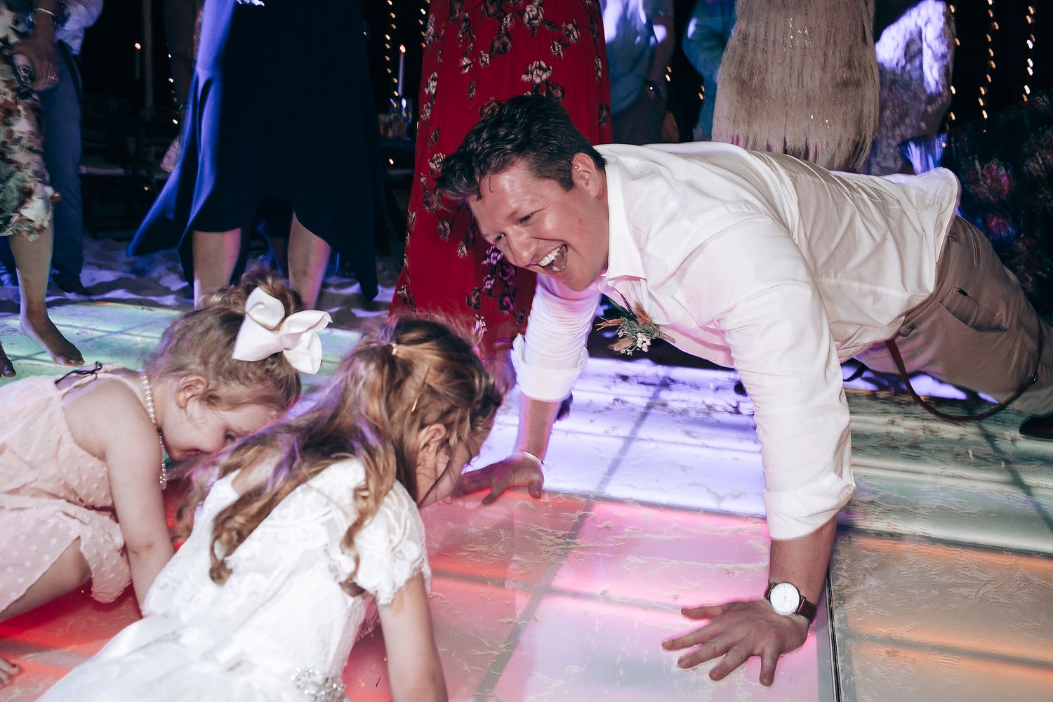 Wedding party dances under colorful lights during evening reception celebration.