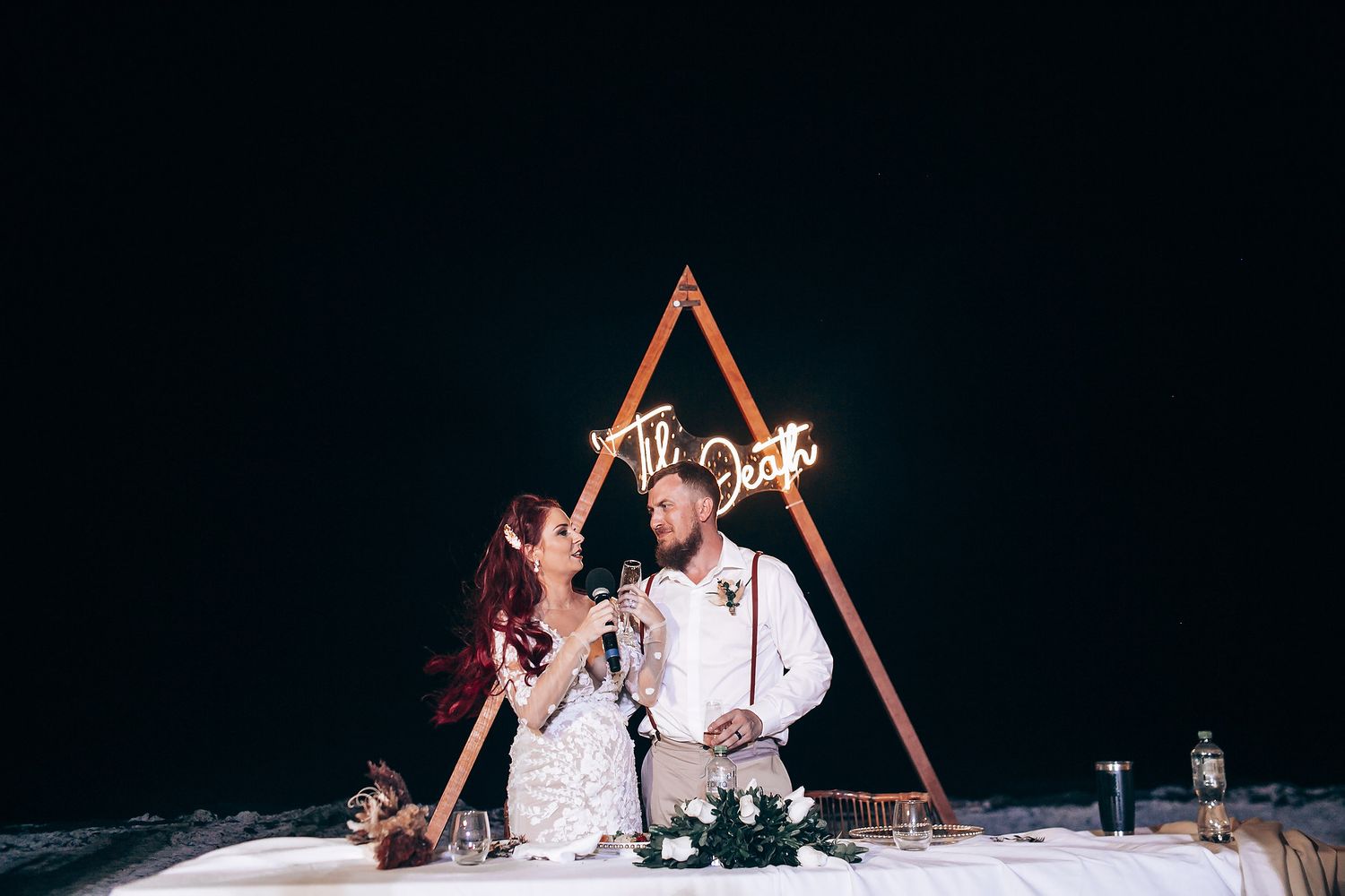 Wedding celebration at night with triangular arch illuminated against dark background.