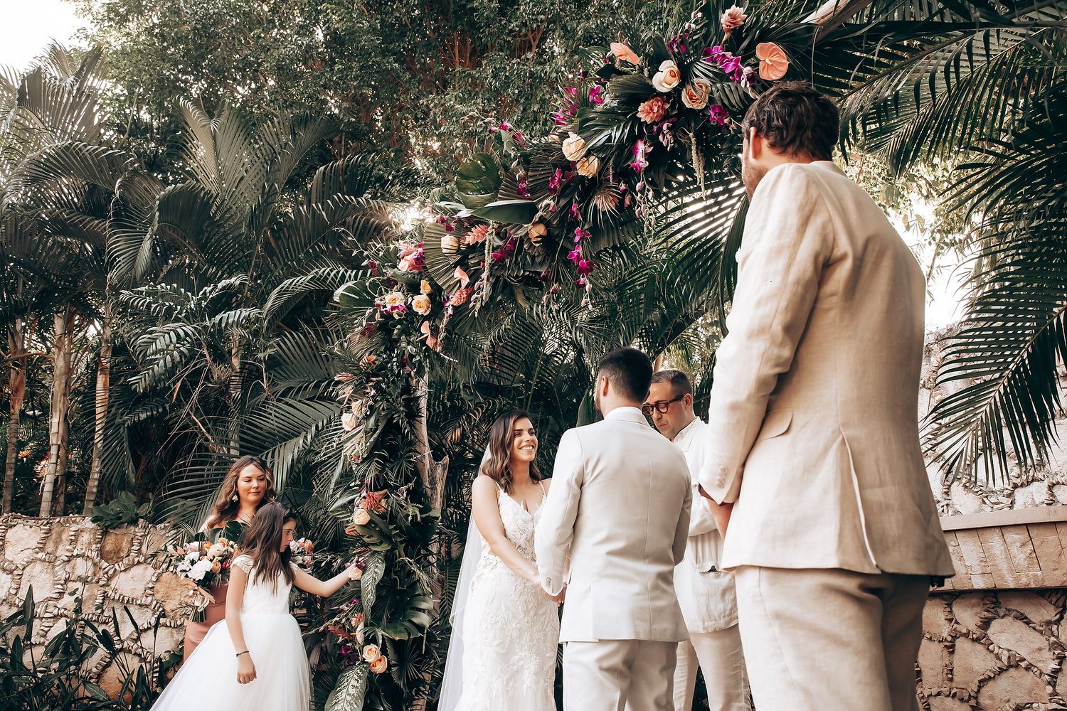 Wedding ceremony gathering with white and floral decor in a tropical garden setting.