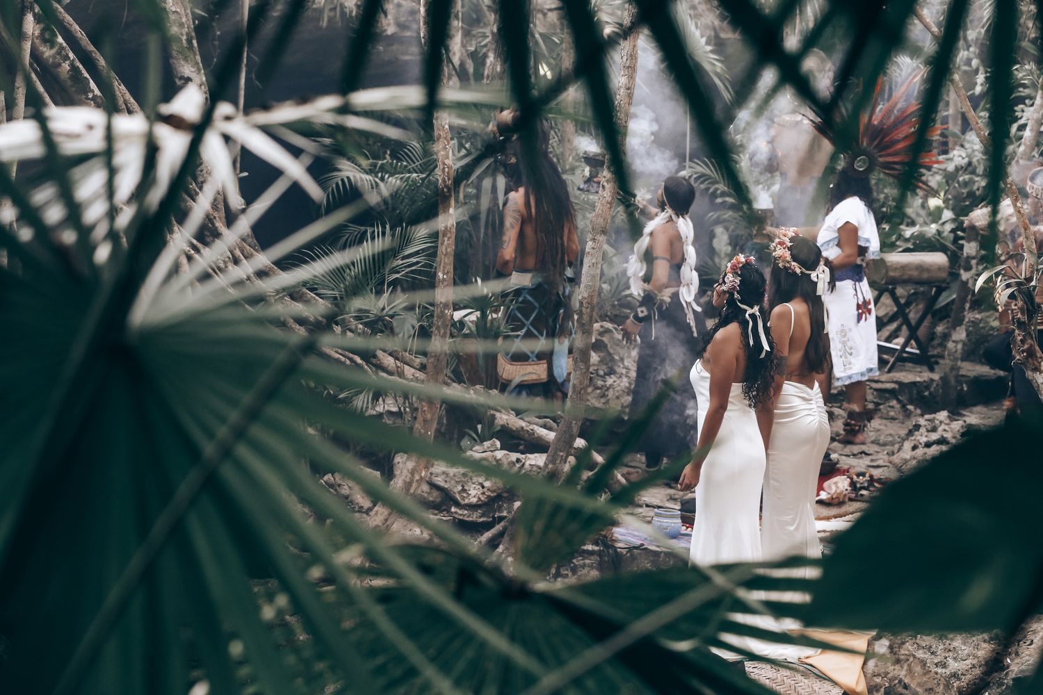 Two figures in flowing white dresses pose together in a natural outdoor setting.