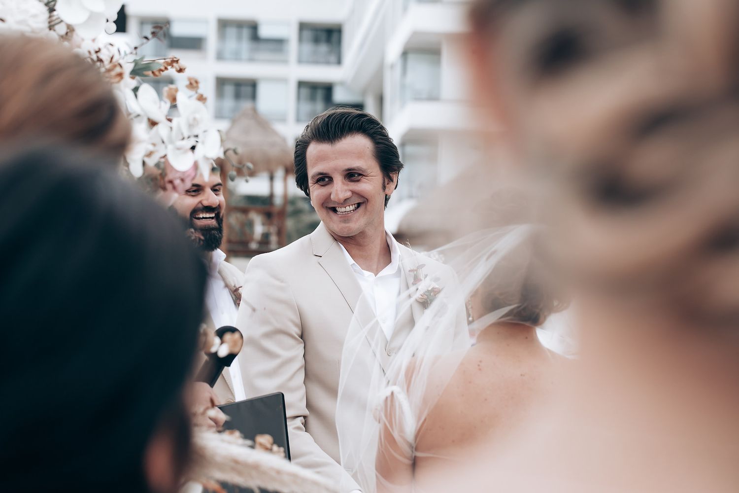 Intimate beach wedding ceremony with guests seated in white chairs by the ocean.