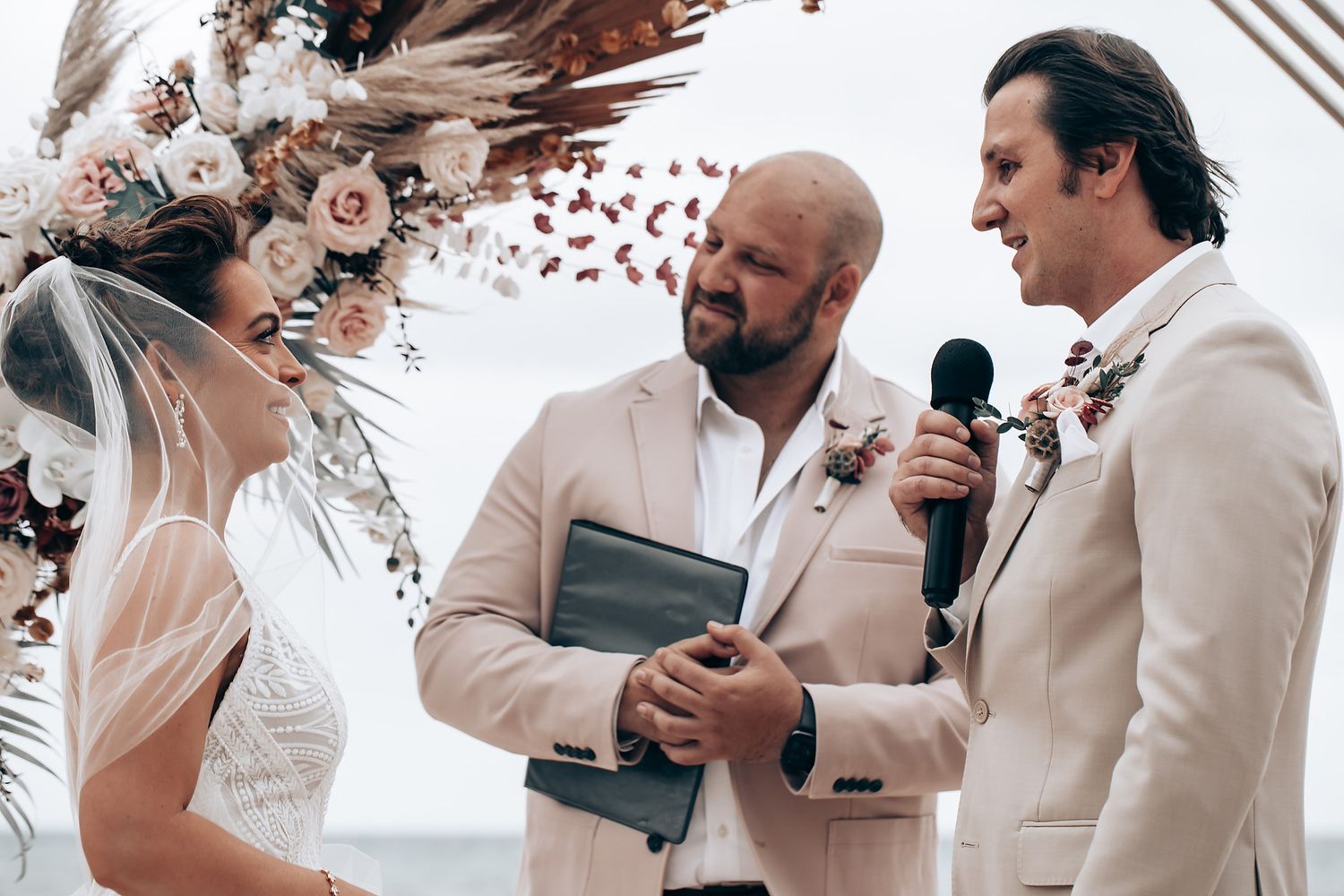 Wedding ceremony scene with guests seated outdoors under floral decorations.