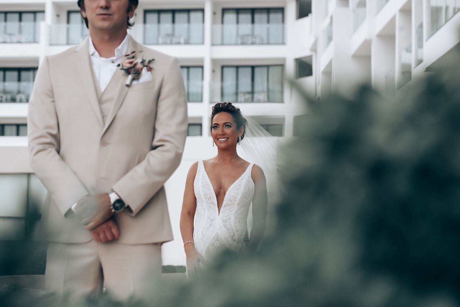 Wedding party members in light beige suits stand outdoors near modern building.