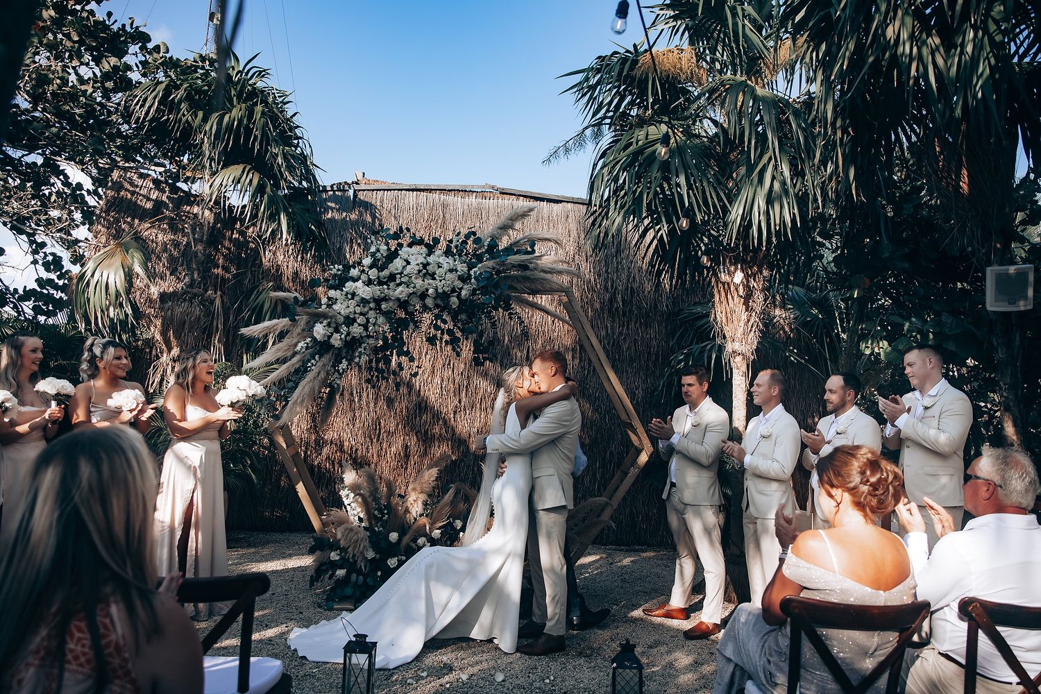 Outdoor wedding ceremony setup with white chairs and palm trees in a tropical setting.