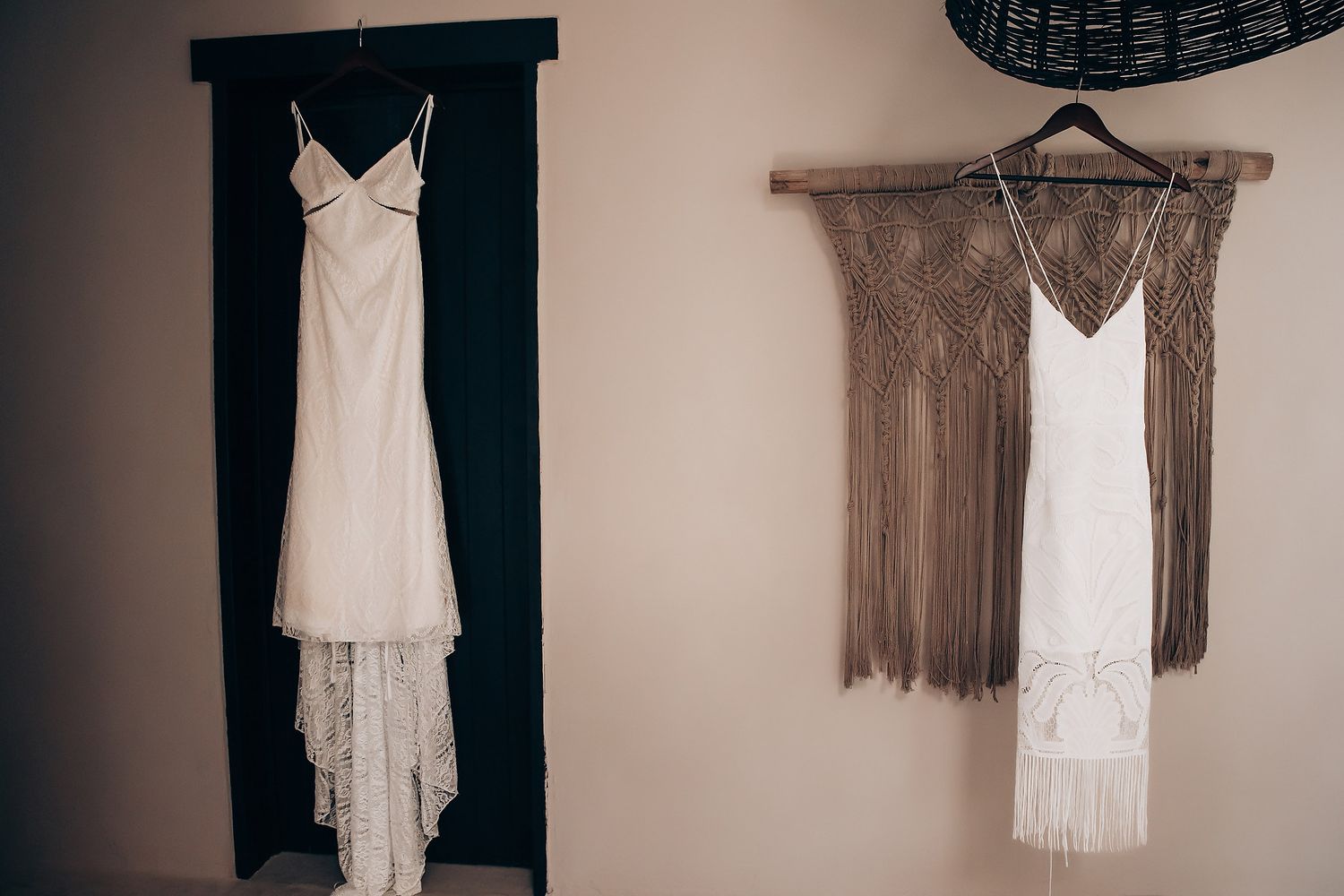 A collection of vintage-style white lace and fringe dresses hanging on hangers against a neutral wall.