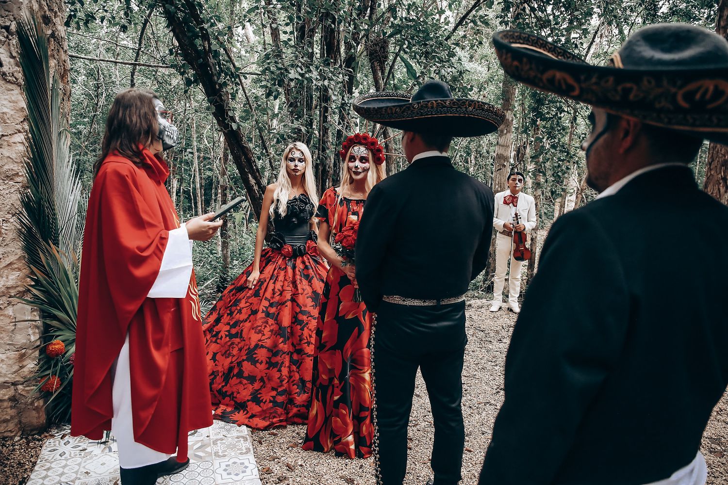 A unique wedding ceremony with red-robed officiant and dramatic red floral dress in a forest setting.