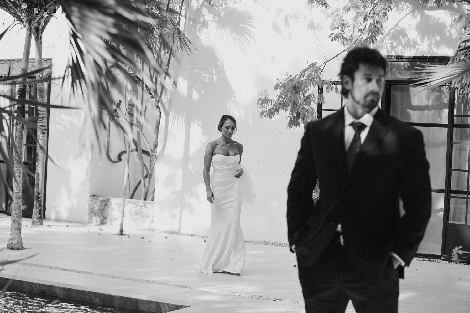 Bride in white gown and groom in black suit pose artistically in black and white wedding photo.