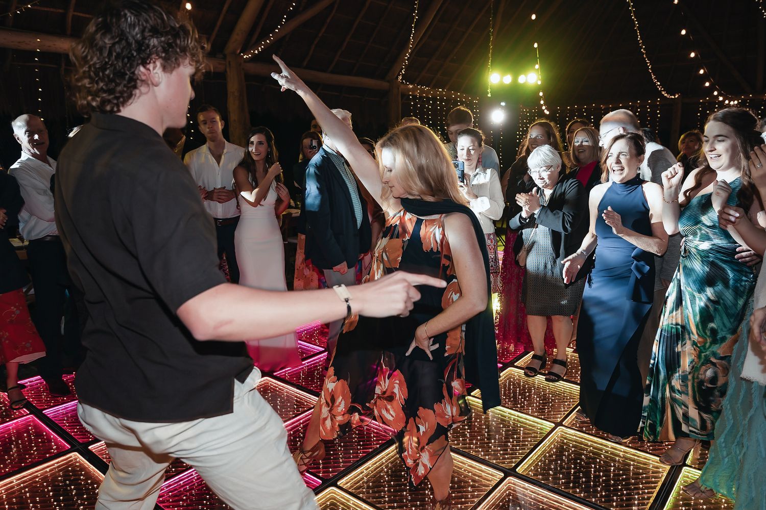 Guests dancing on a illuminated dance floor at an elegant outdoor wedding reception under a decorated tent.