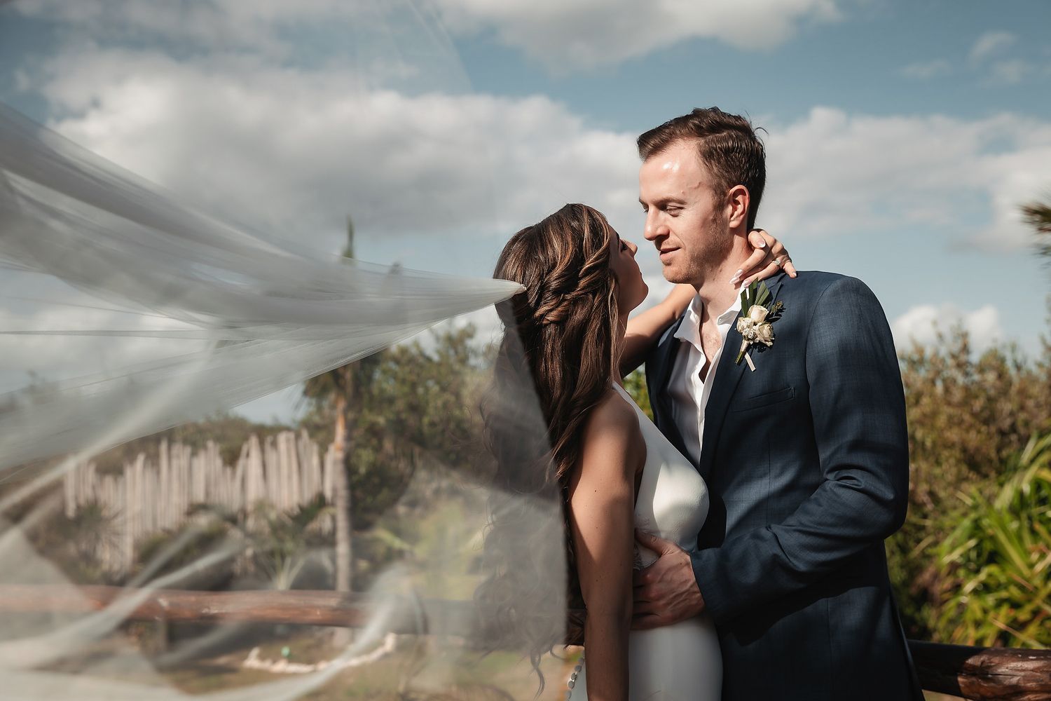 Romantic couple embracing outdoors with bride's veil flowing in the wind on their wedding day.