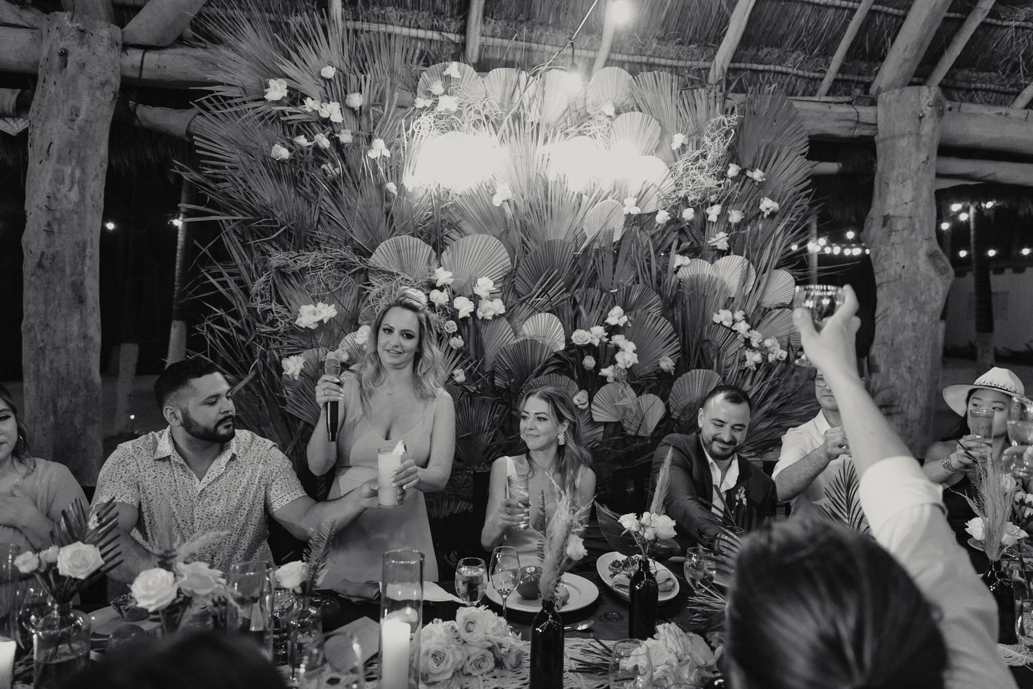 Black and white photo of wedding party guests laughing and celebrating at tropical reception dinner.