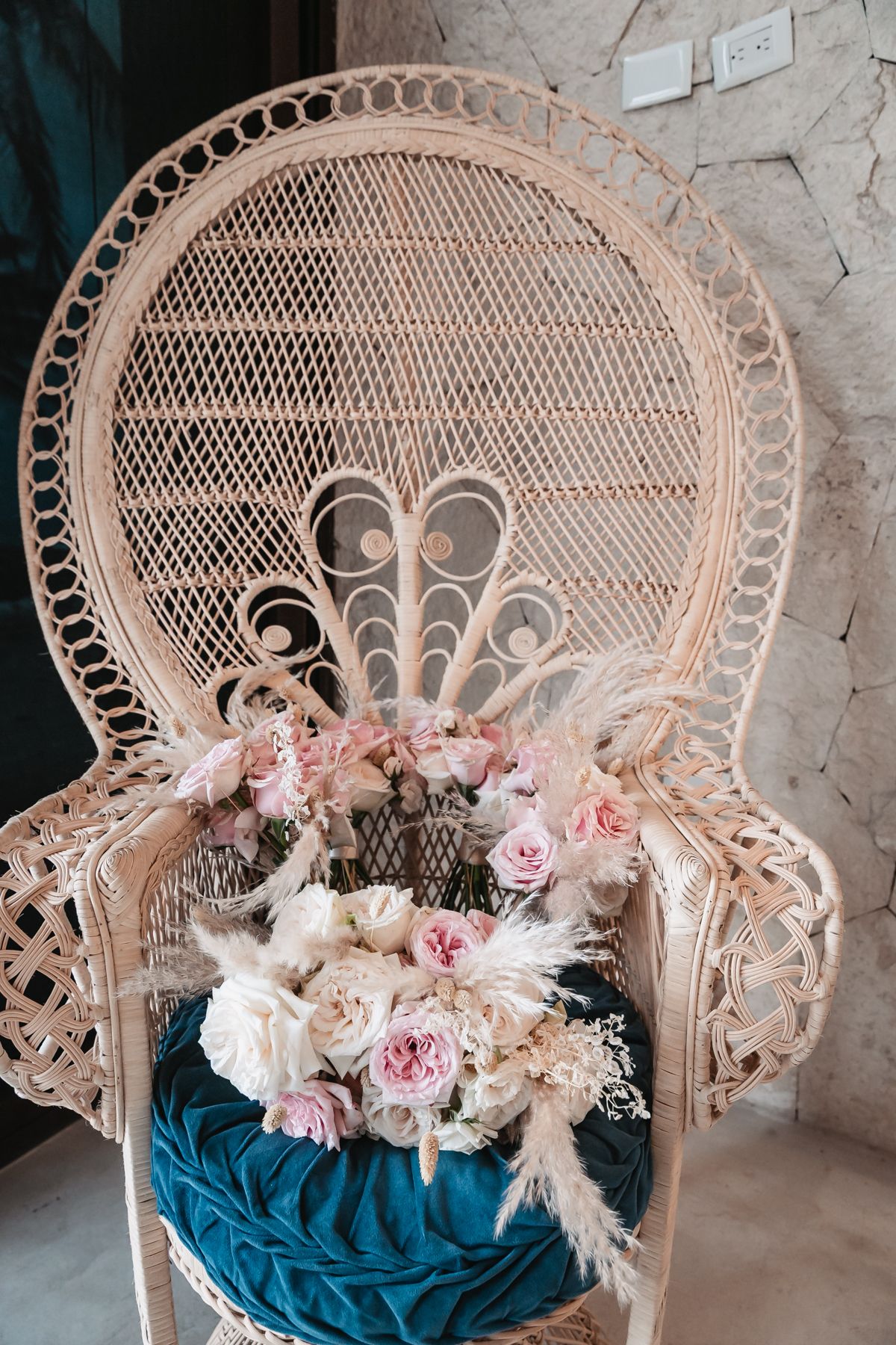 Elegant peacock wicker chair with a bohemian bridal bouquet of pink roses and pampas grass on a teal velvet cushion.