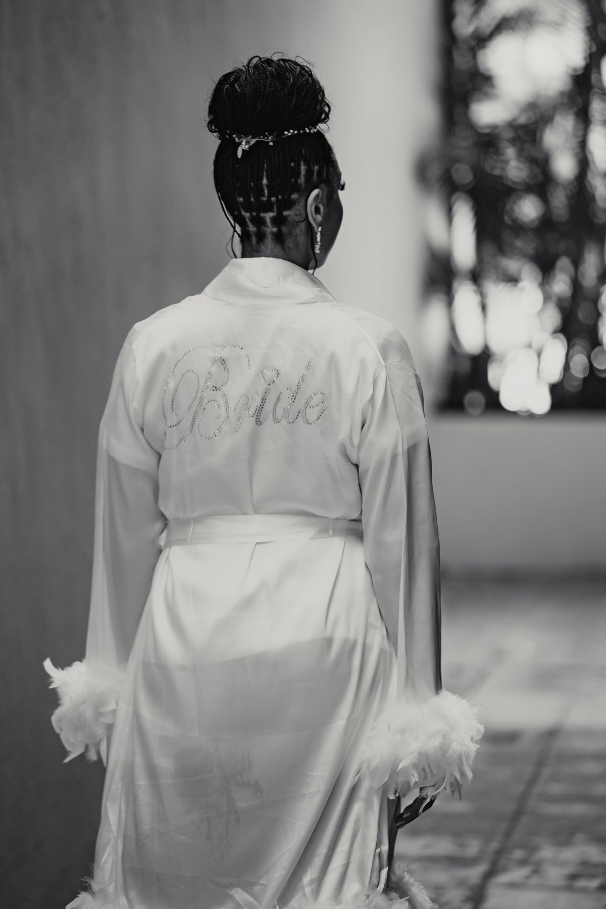 Black and white photo of a bride wearing a white feather-trimmed robe with Bride written on the back.