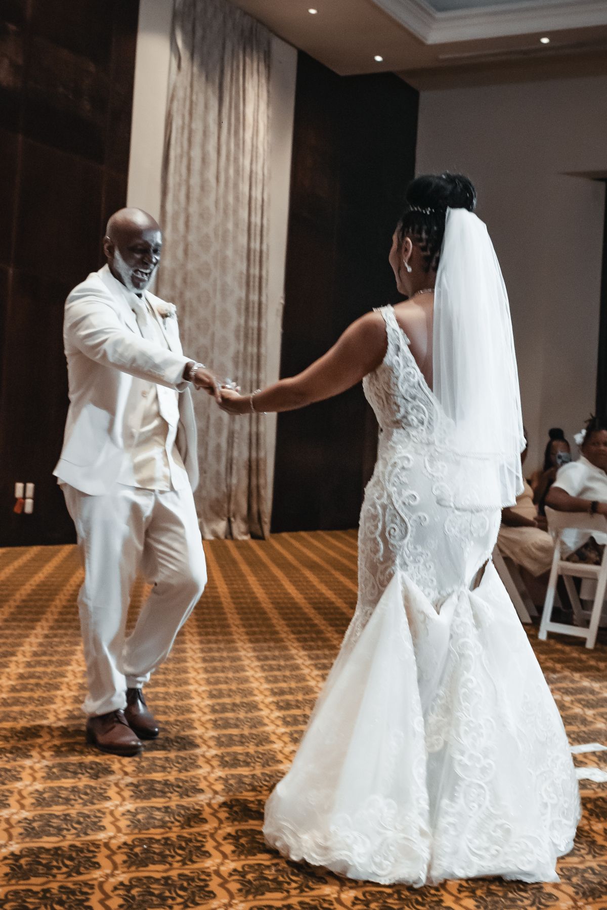 Bride and groom share their first dance in elegant white wedding attire at a formal ballroom reception.
