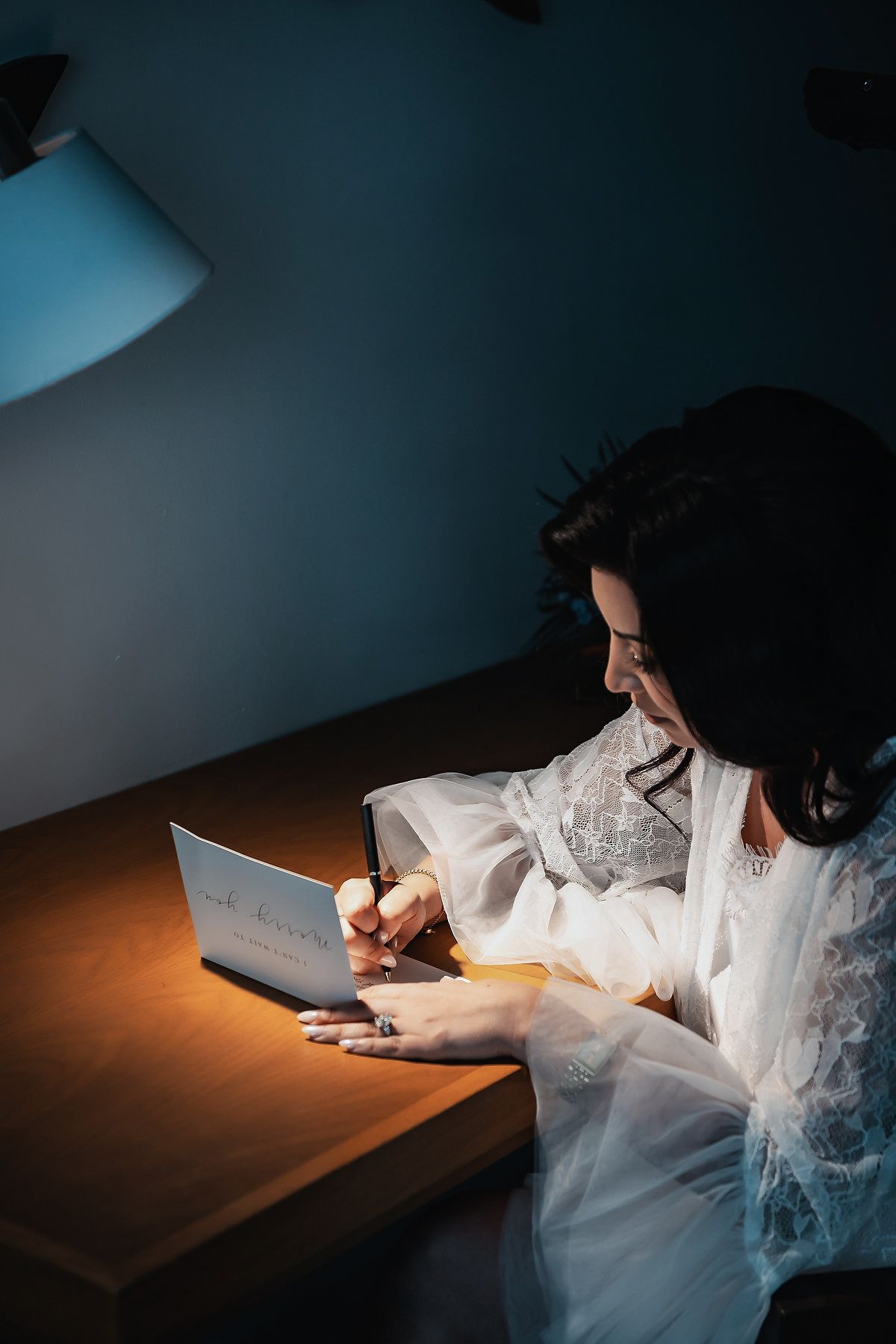 Woman in white robe writing notes by laptop at dimly lit wooden desk at night.