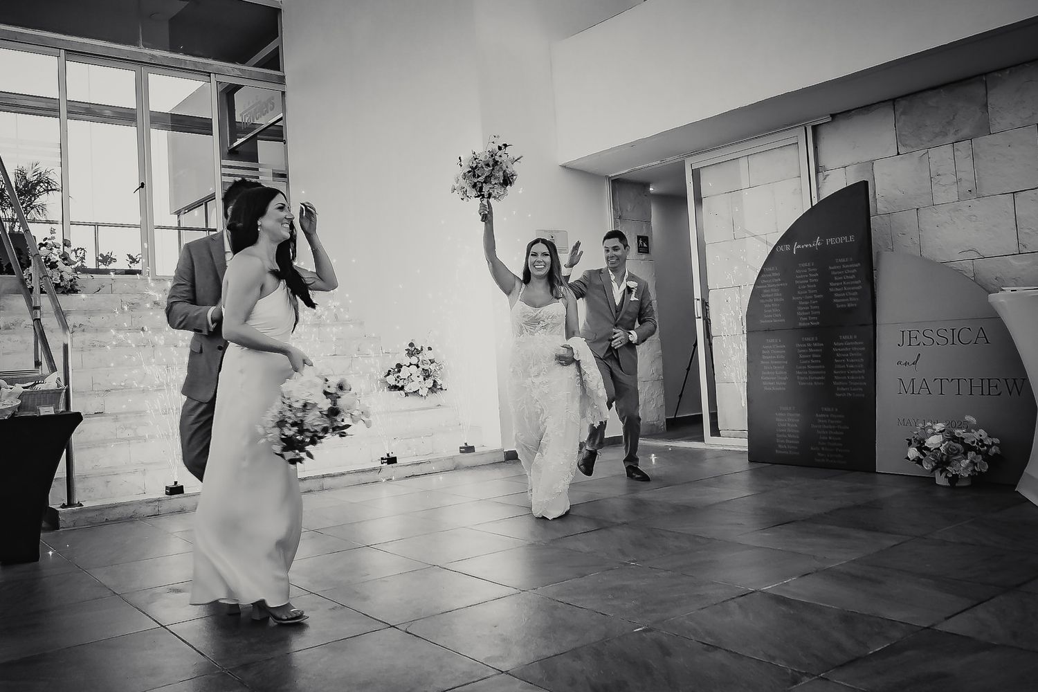 Black and white wedding photo of bride and groom making grand entrance with bouquet raised in celebration.