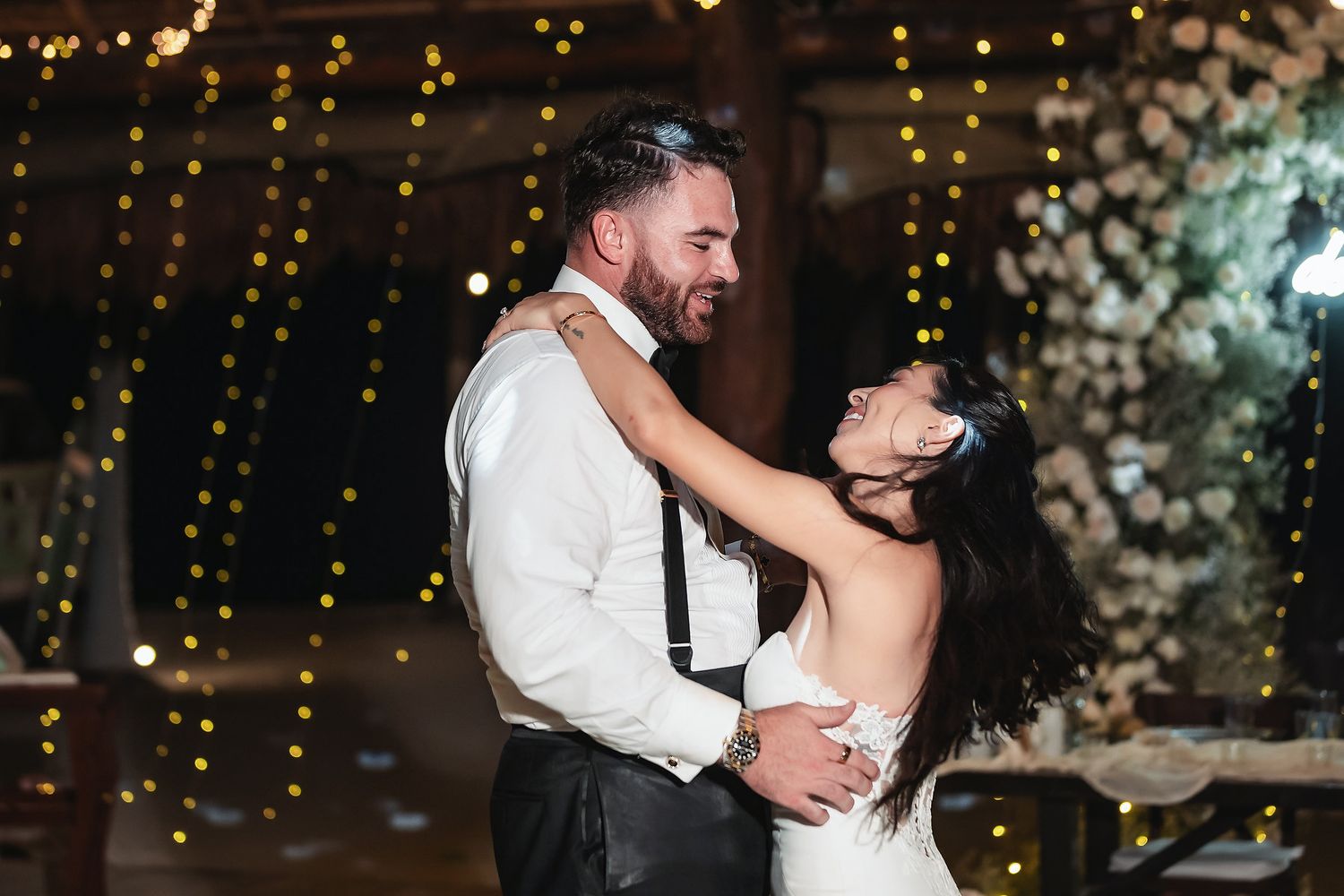 Couple sharing first dance at romantic wedding reception with fairy lights and floral backdrop.