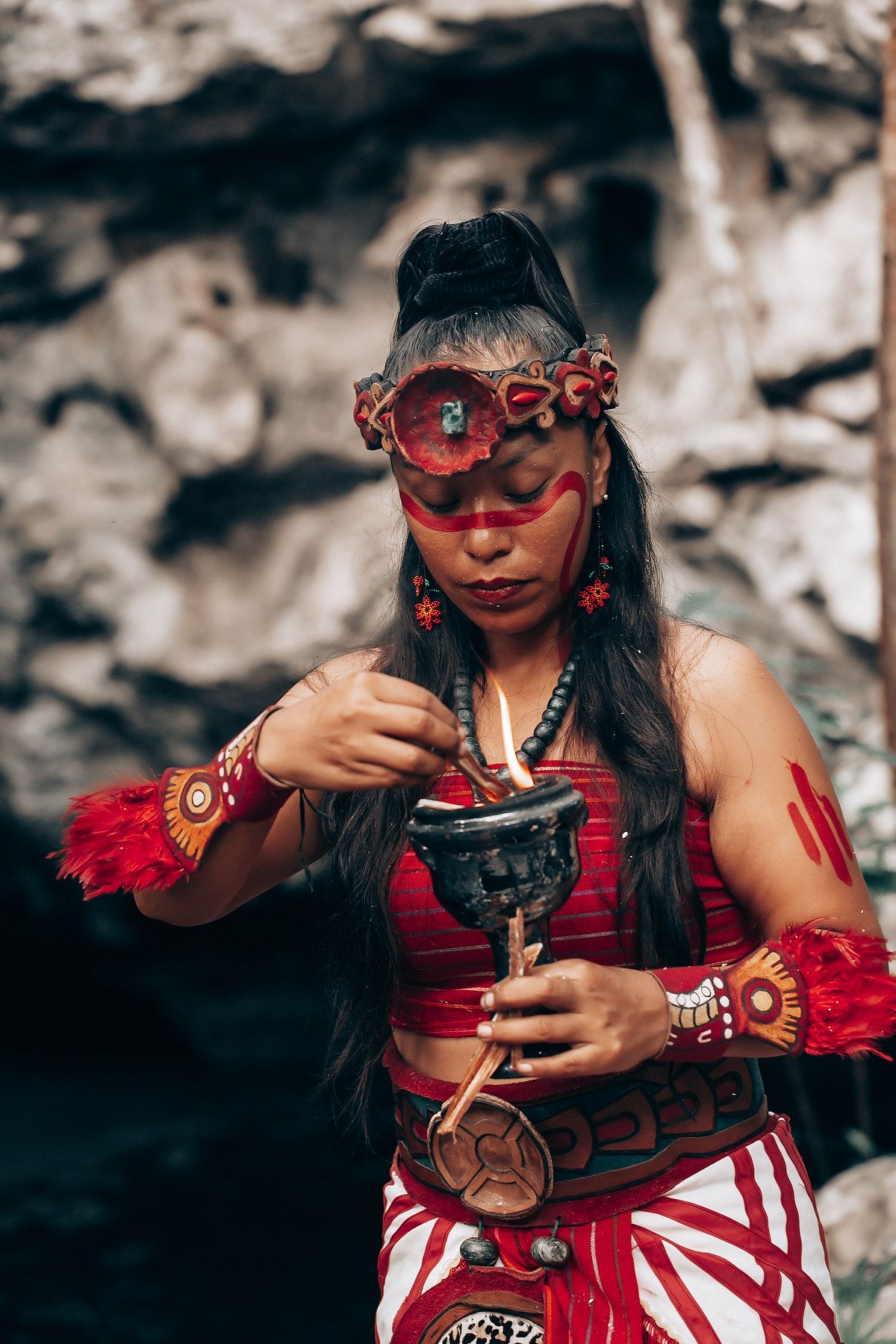 Woman in red and white traditional dress performing a ritual ceremony with decorative accessories.