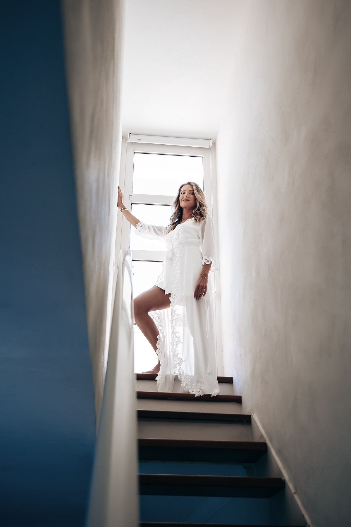 A woman in a white wedding dress is standing in a doorway, with natural light streaming in.