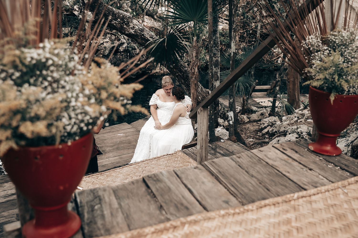 A woman in a white dress sitting on a wooden deck surrounded by lush greenery and potted plants.