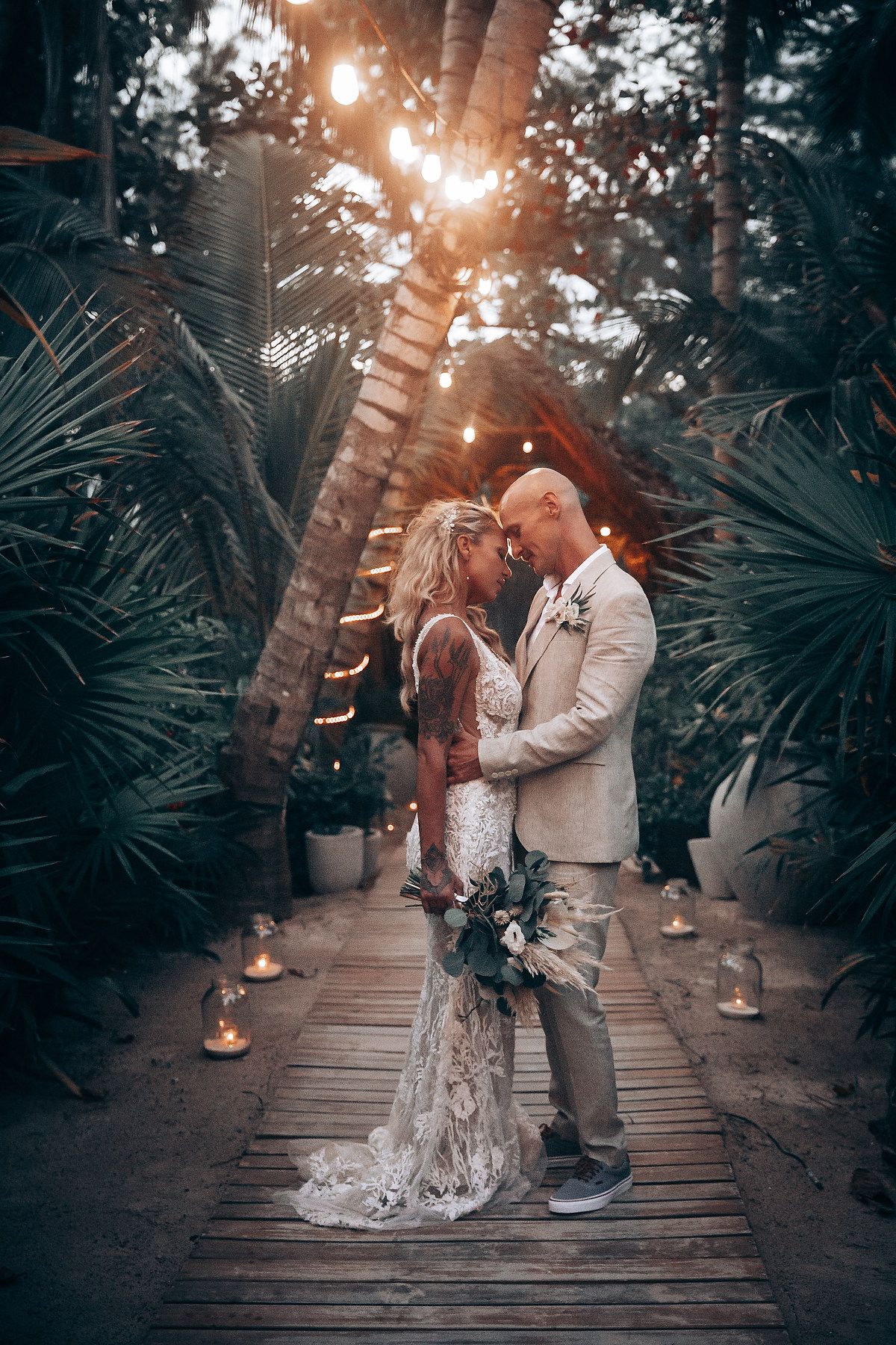 Romantic sunset moment on a wooden boardwalk surrounded by tropical plants and string lights.