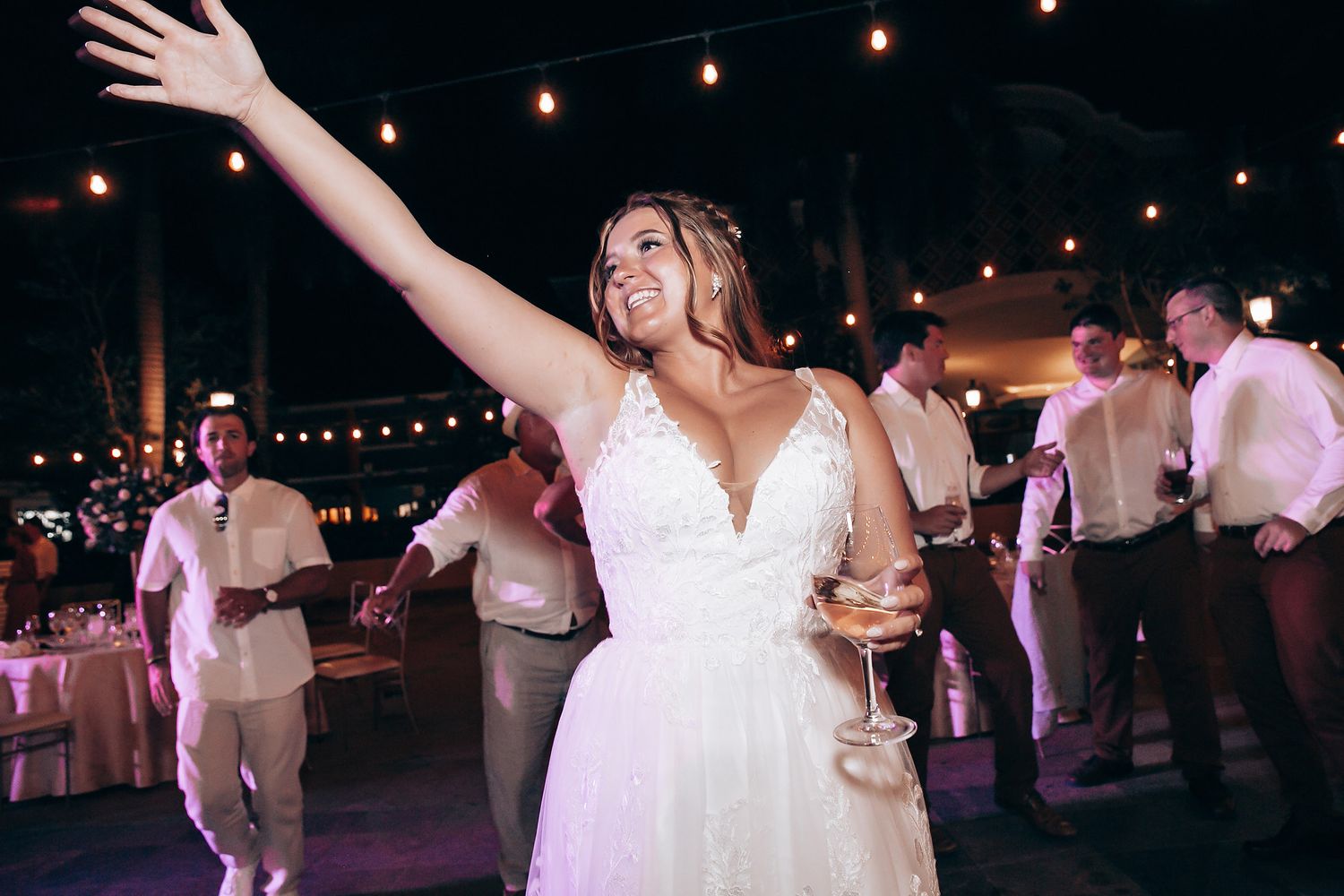 Wedding celebration with a person in white dress dancing under string lights at night.